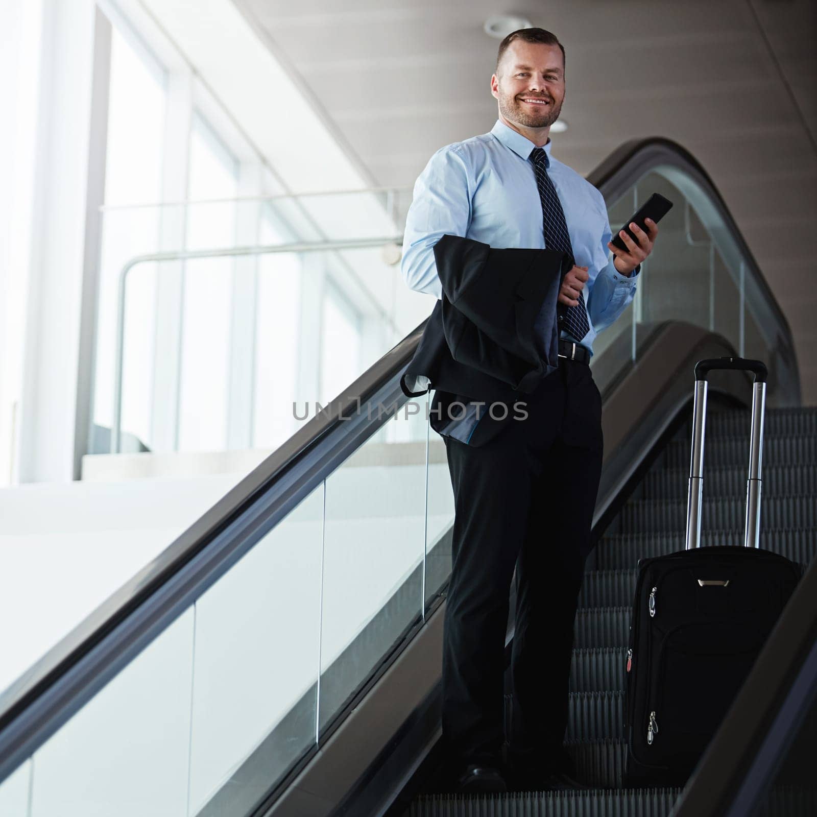 Making business travel an enjoyable experience. a businessman traveling down an escalator in an airport. by YuriArcurs