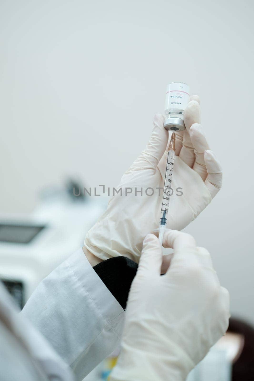 Cosmetologist putting mesotherapy serum on syringe from serum bottle by danjelaruci