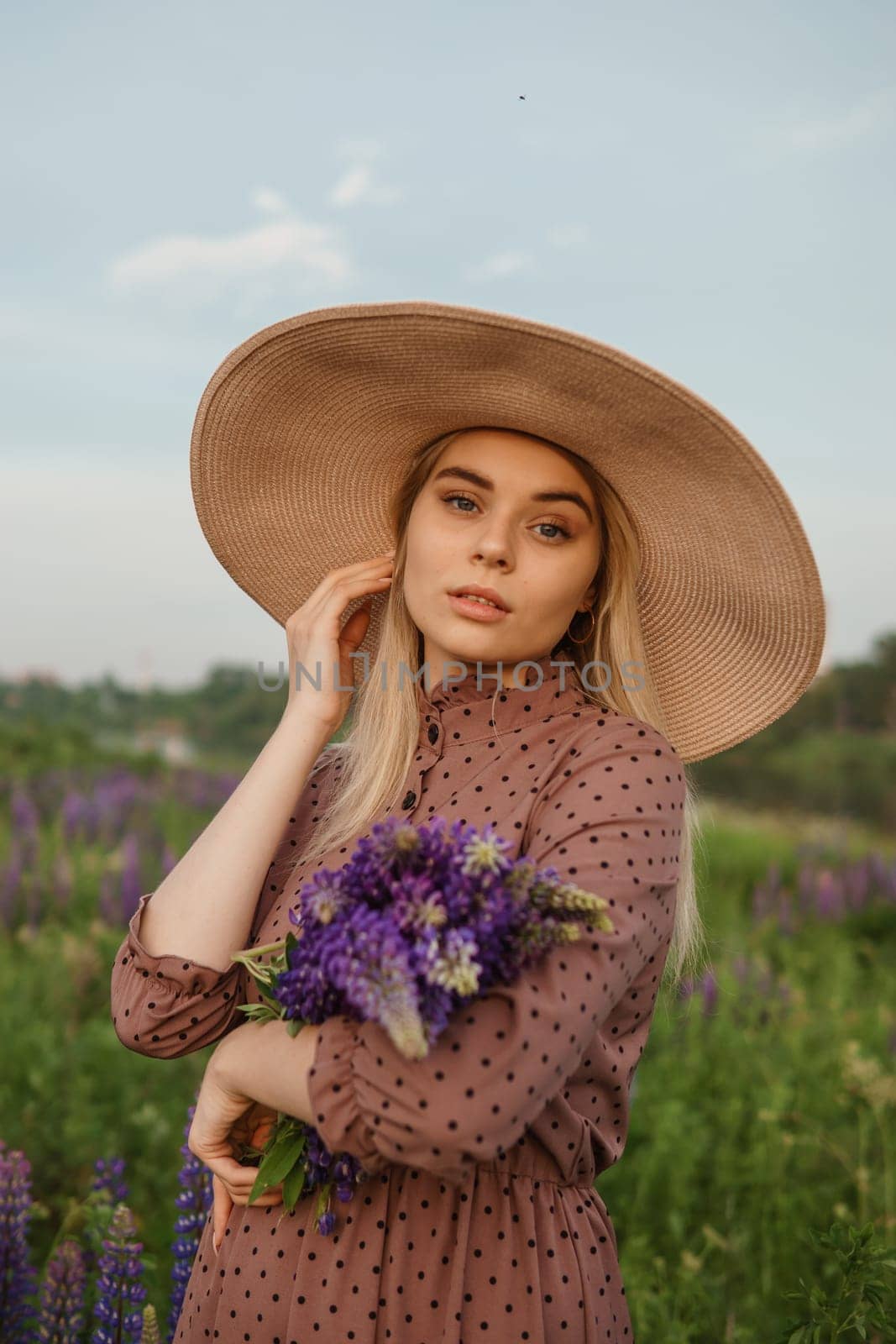 A beautiful woman in a straw hat walks in a field with purple flowers. A walk in nature in the lupin field by Annu1tochka