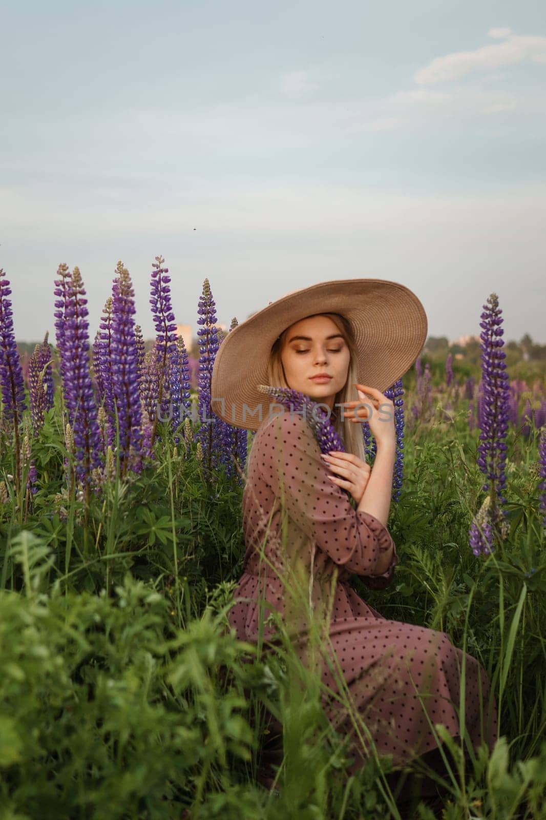 A beautiful woman in a straw hat walks in a field with purple flowers. A walk in nature in the lupin field by Annu1tochka