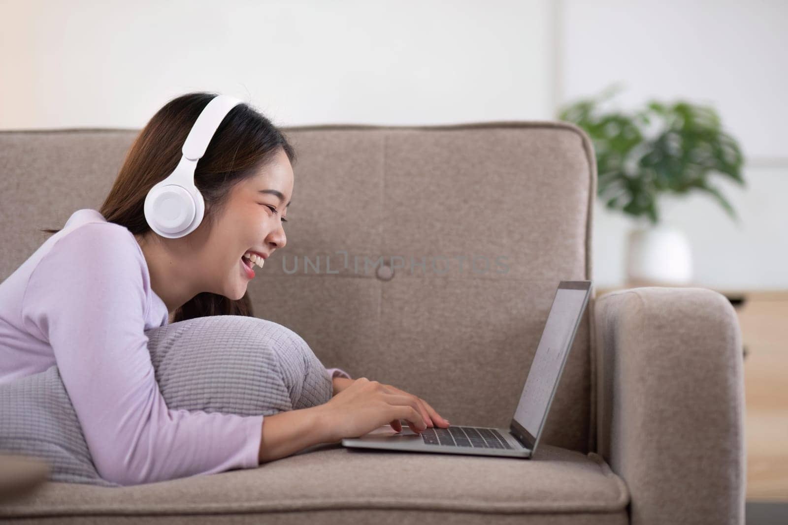 Young asian girl using laptop working call video conference with her friend in living room at home. Happy young Asian girl relaxing at home.