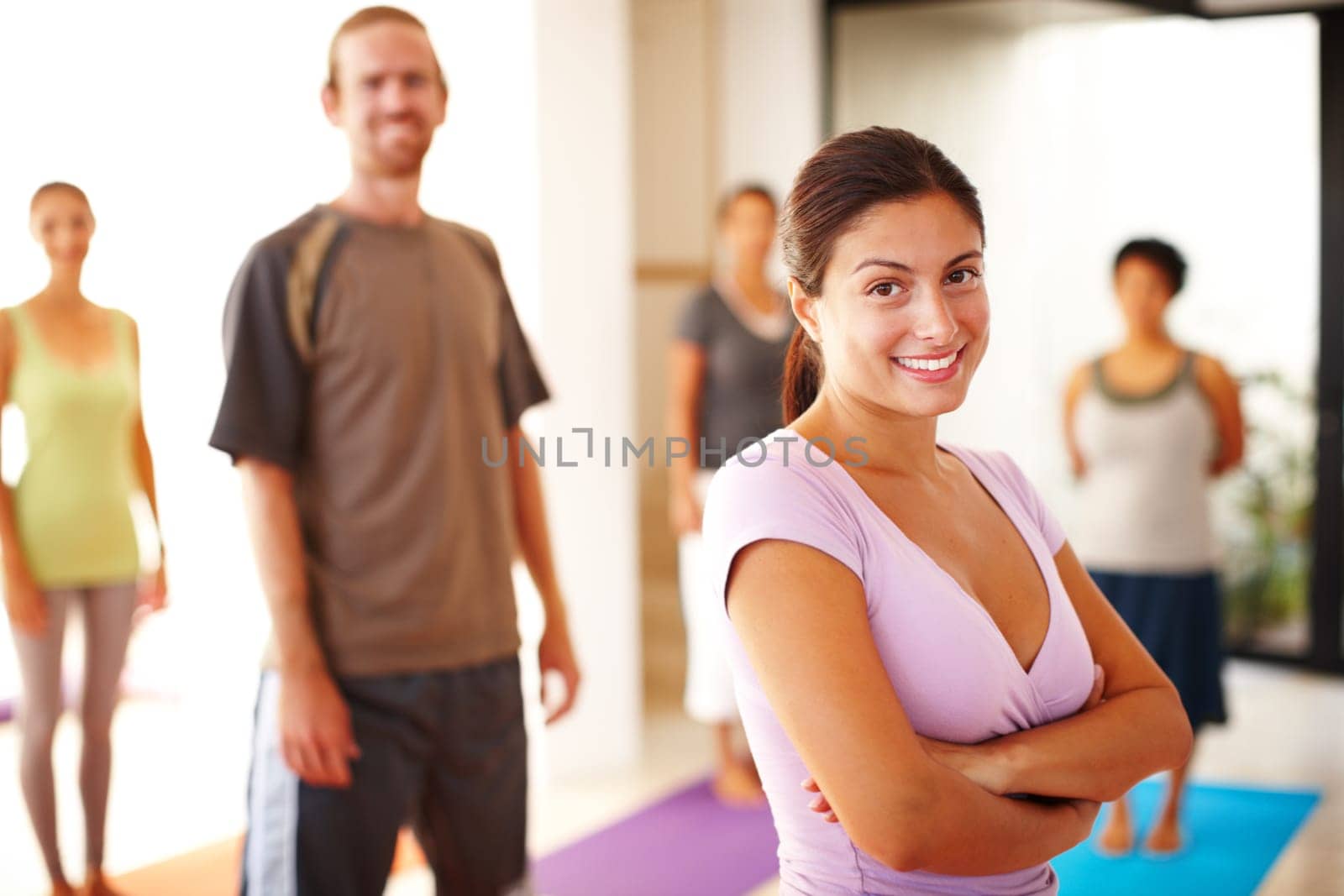 Leader of the yoga pack. A gorgeous young yoga instructor stands in front of her class with arms crossed
