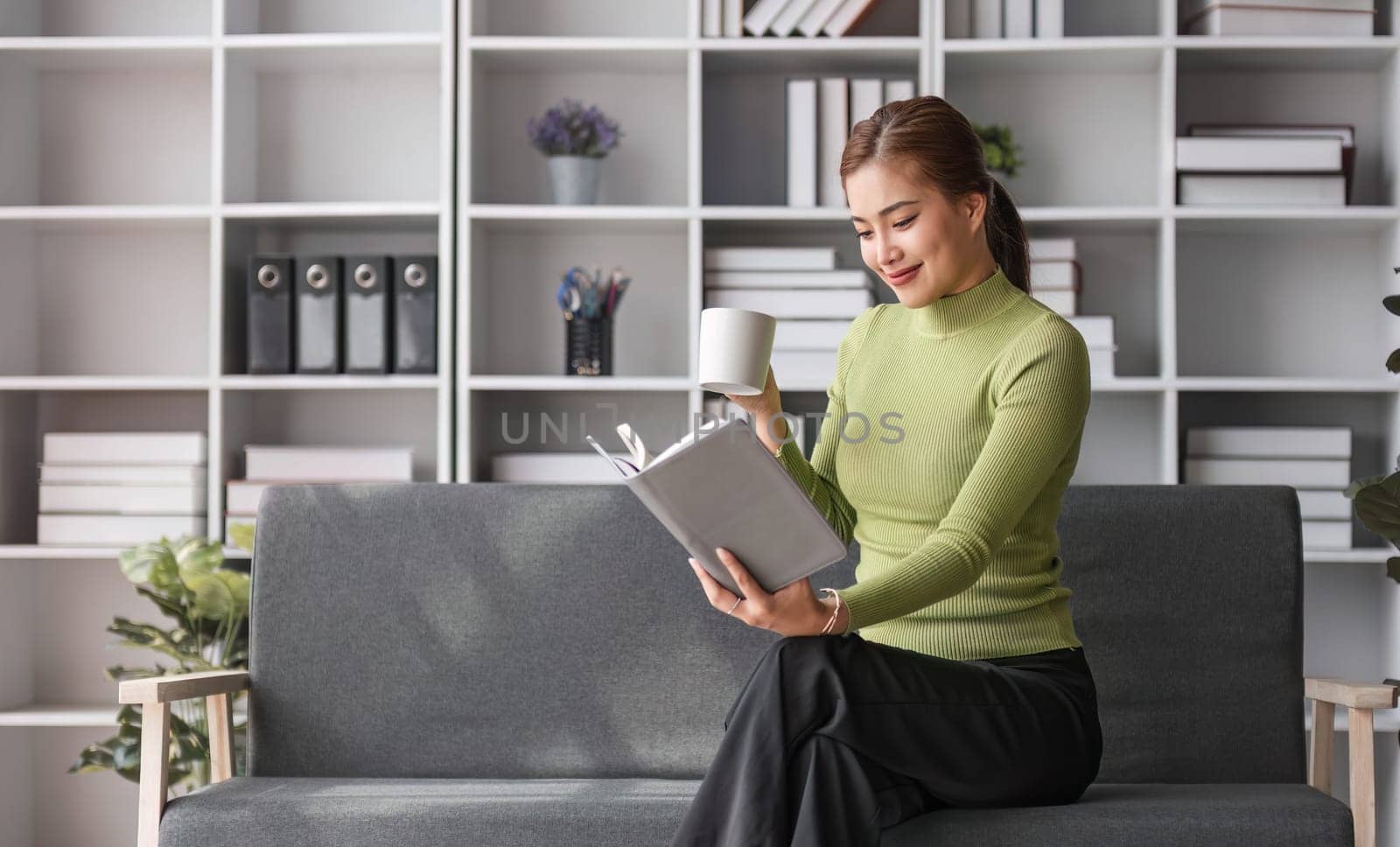 Attractive young Asian woman sits in the minimal and comfortable living room enjoying reading a book...