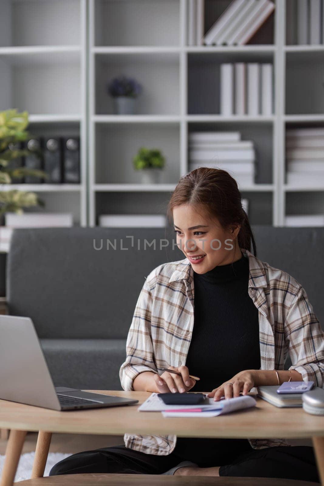 Beautiful and inspired Asian woman working on her tasks on laptop in a living room on the weekend...