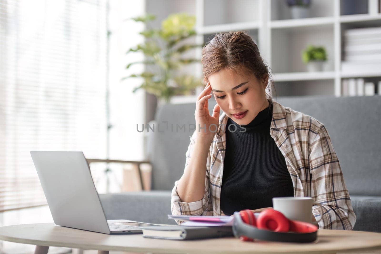 Stressed young Asian female college student preparing for the exam, reading documents at a coffee table in her living room...