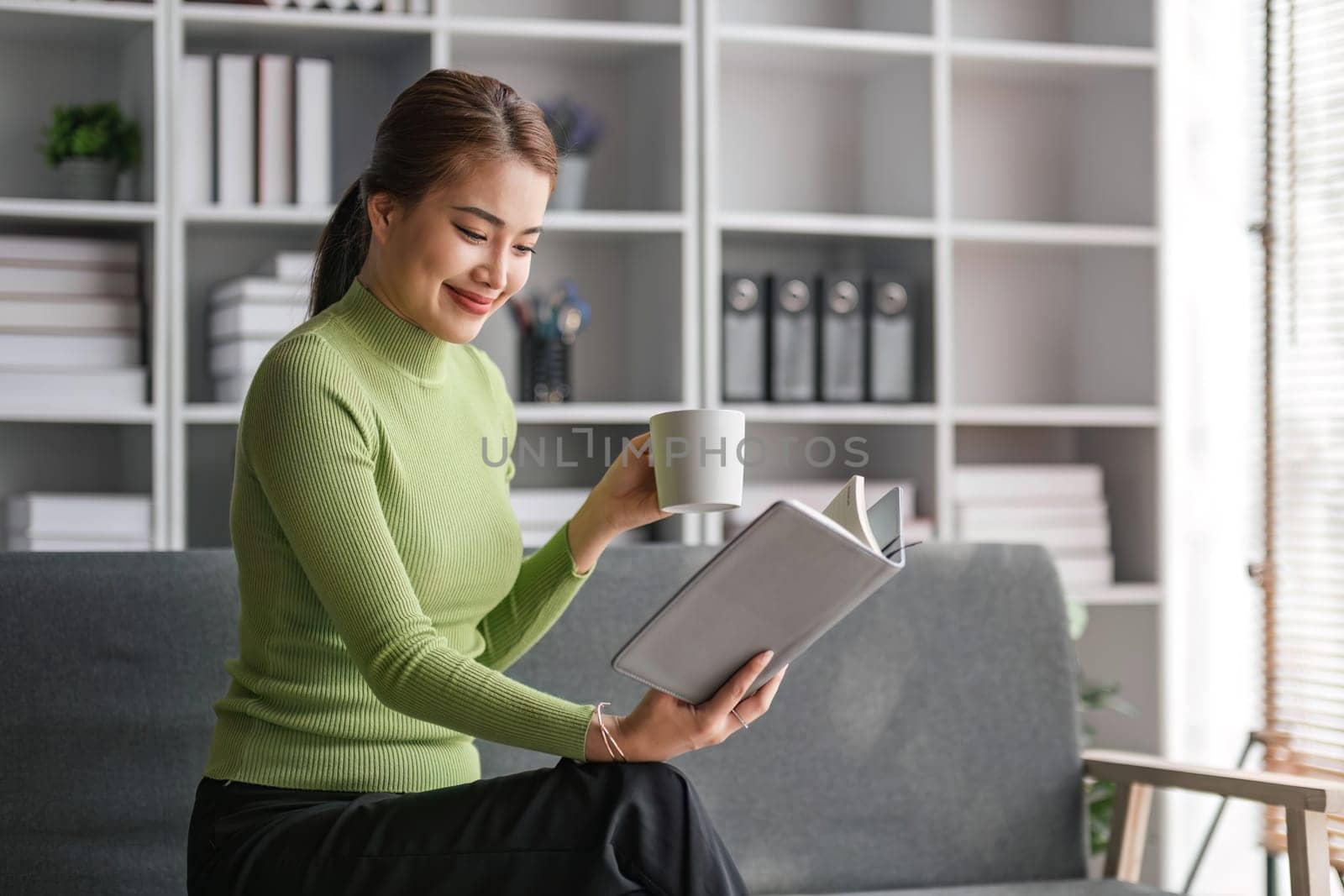 Attractive young Asian woman sits in the minimal and comfortable living room enjoying reading a book...