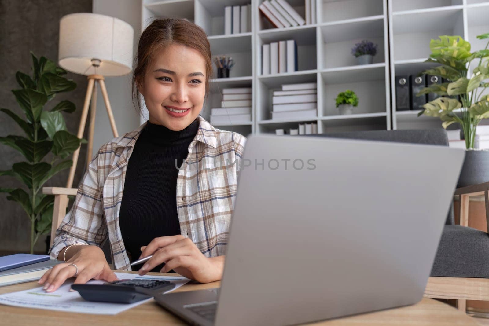 Beautiful and inspired Asian woman working on her tasks on laptop in a living room on the weekend...