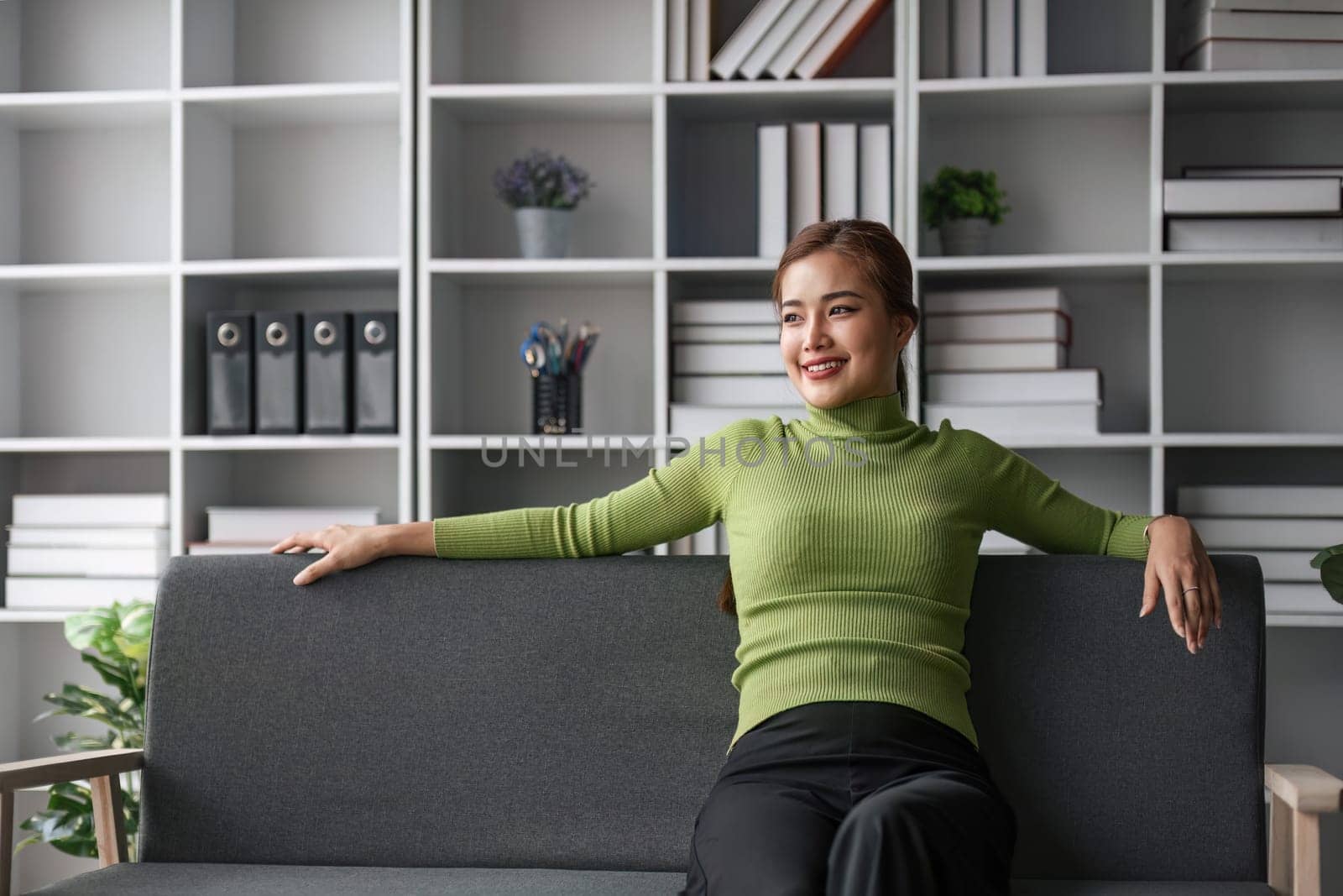 Attractive young Asian woman sits in the minimal and comfortable living room enjoying reading a book...