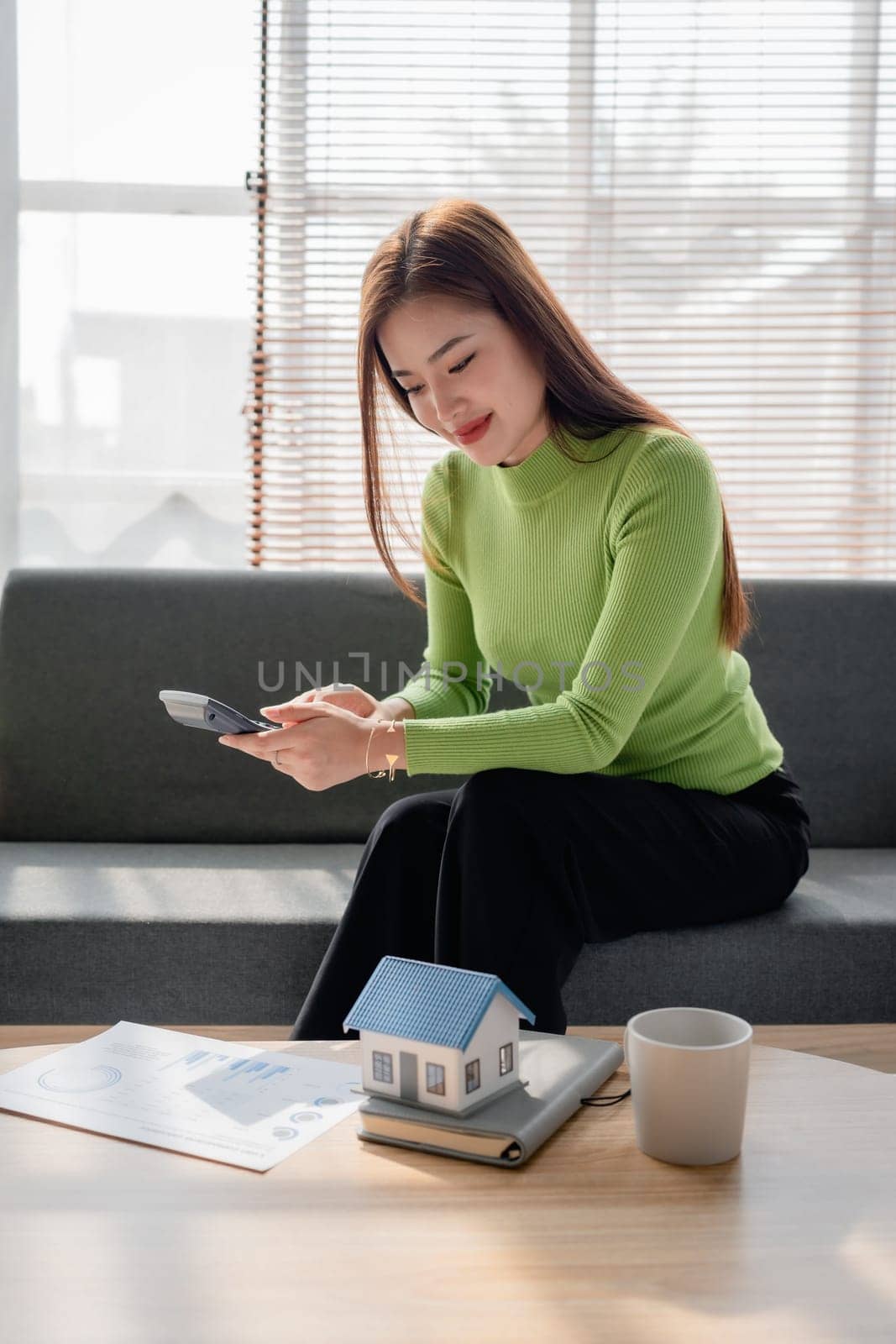 woman sitting on cozy sofa and planning and calculate expense and mortgage with calculator and home on desk, insurance and budget of residential, loan and residence, business and property concept