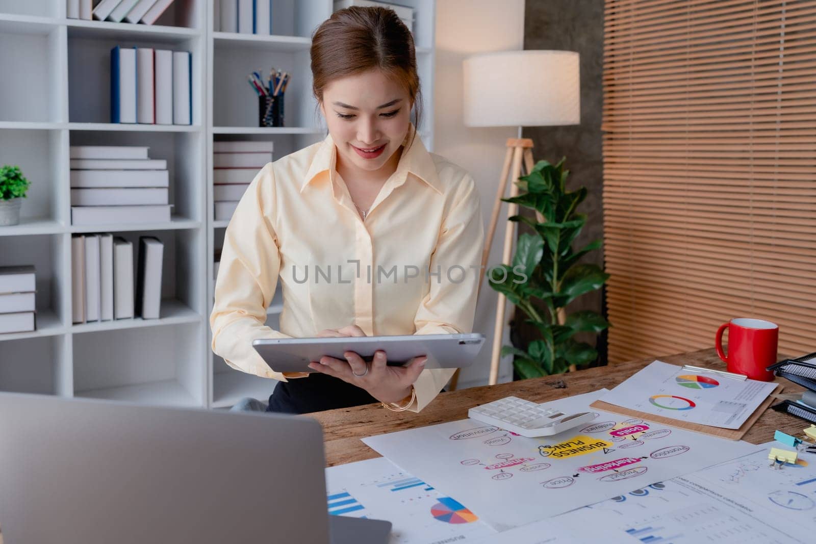 businesswoman in a black suit inside the office using tablet computer, audit paperwork for customers to contact, business people concept