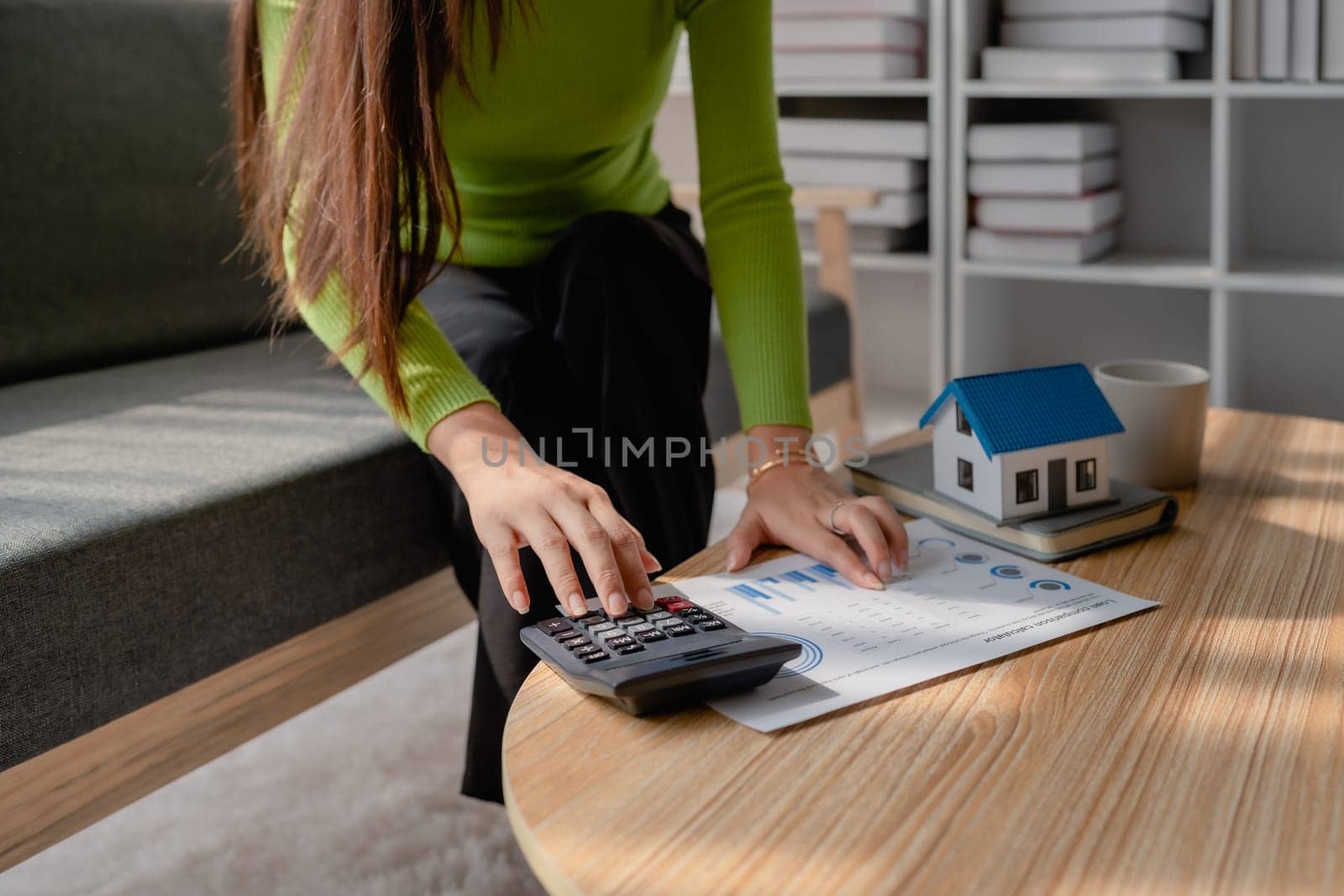 woman sitting on cozy sofa and planning and calculate expense and mortgage with calculator and home on desk, insurance and budget of residential, loan and residence, business and property concept