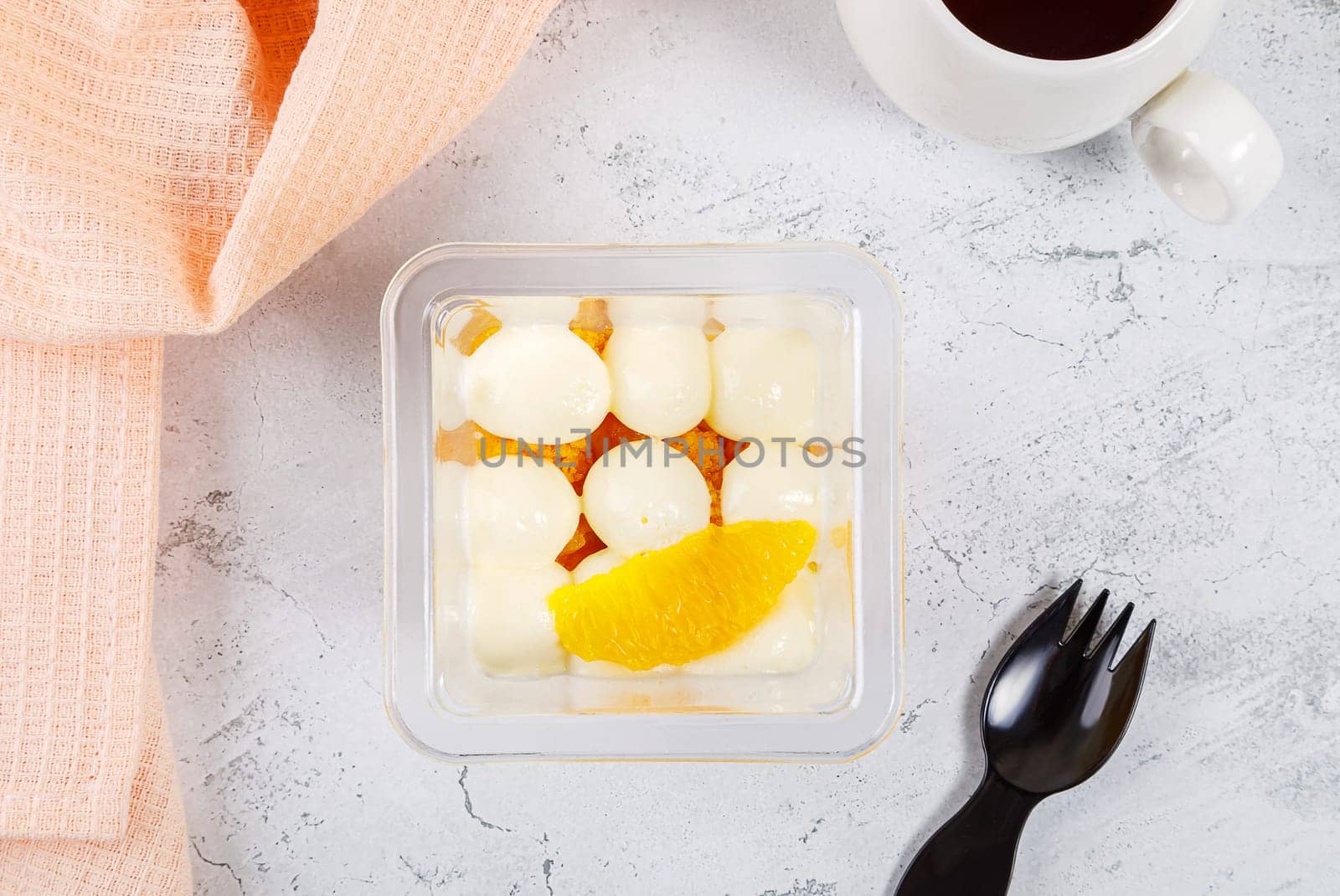 Dessert of cream, jam and orange in a plastic glass on a concrete background. High quality photo