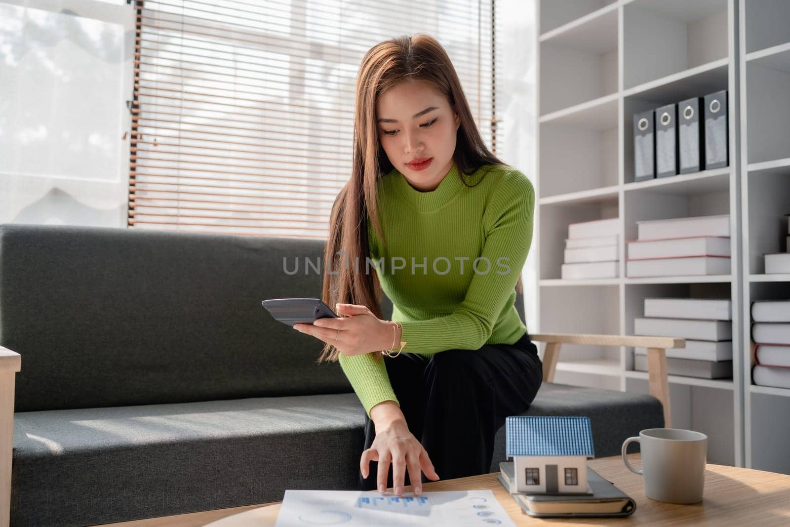 woman sitting on cozy sofa and planning and calculate expense and mortgage with calculator and home on desk, insurance and budget of residential, loan and residence, business and property concept