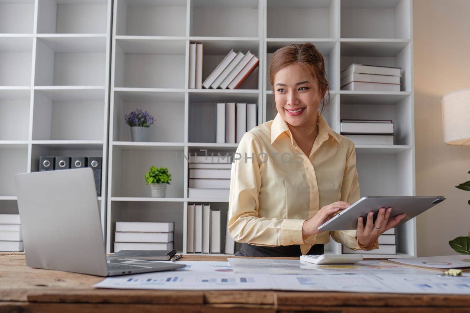 Beautiful and happy young Asian businesswoman looking at her laptop screen while enjoying her morning coffee at her desk in the office...