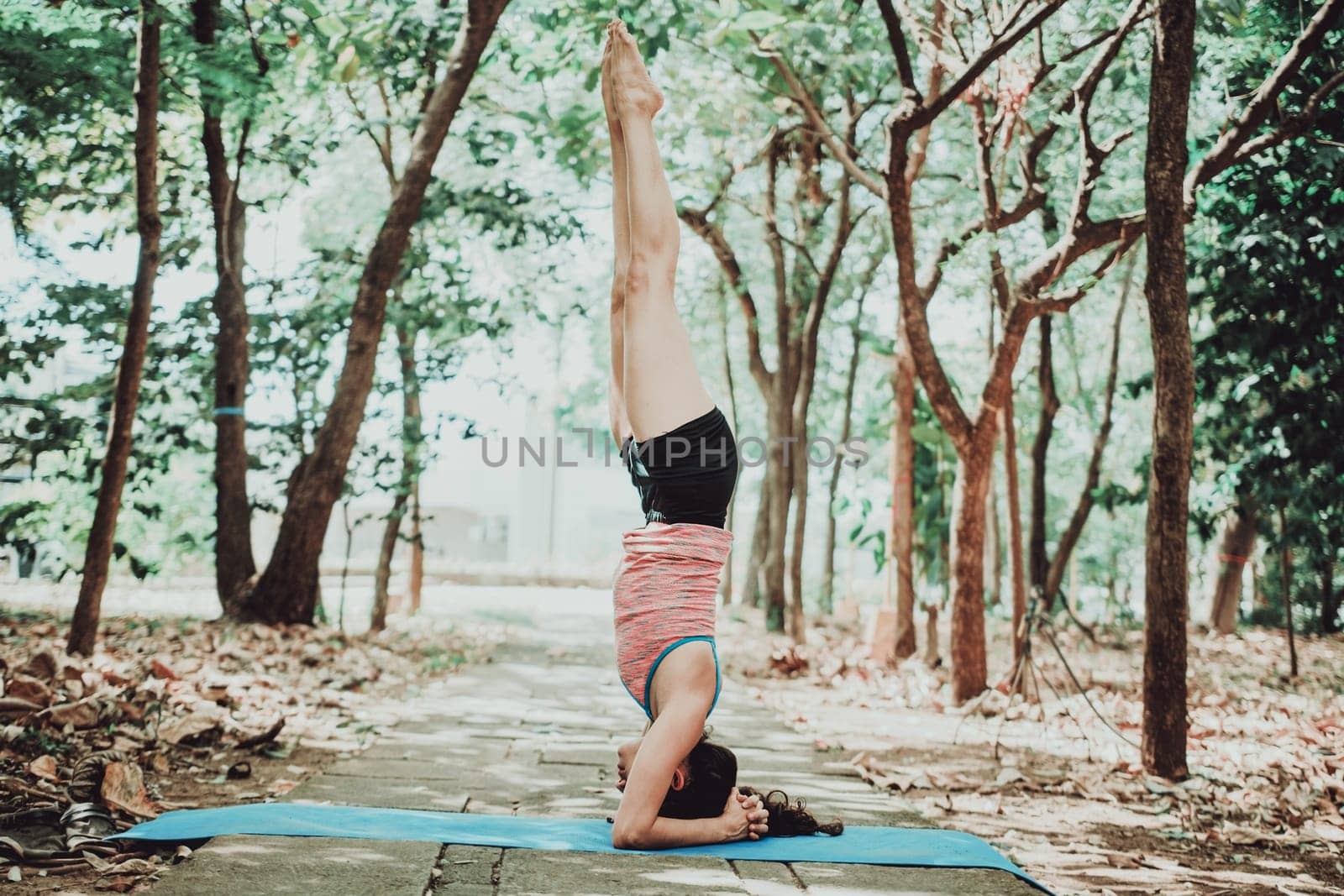Young woman doing headstand yoga outdoors. Spiritual girl practicing yoga sirshasana outdoors. by isaiphoto