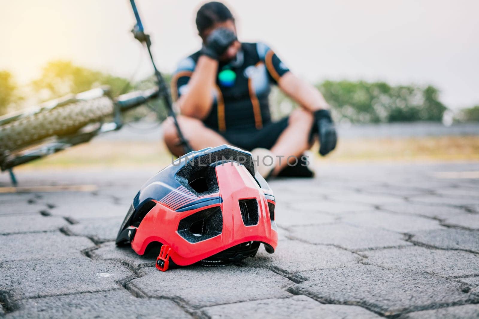 Accidented cyclist sitting on the pavement. Concept of crashed cyclist with helmet on the pavement in first focus by isaiphoto