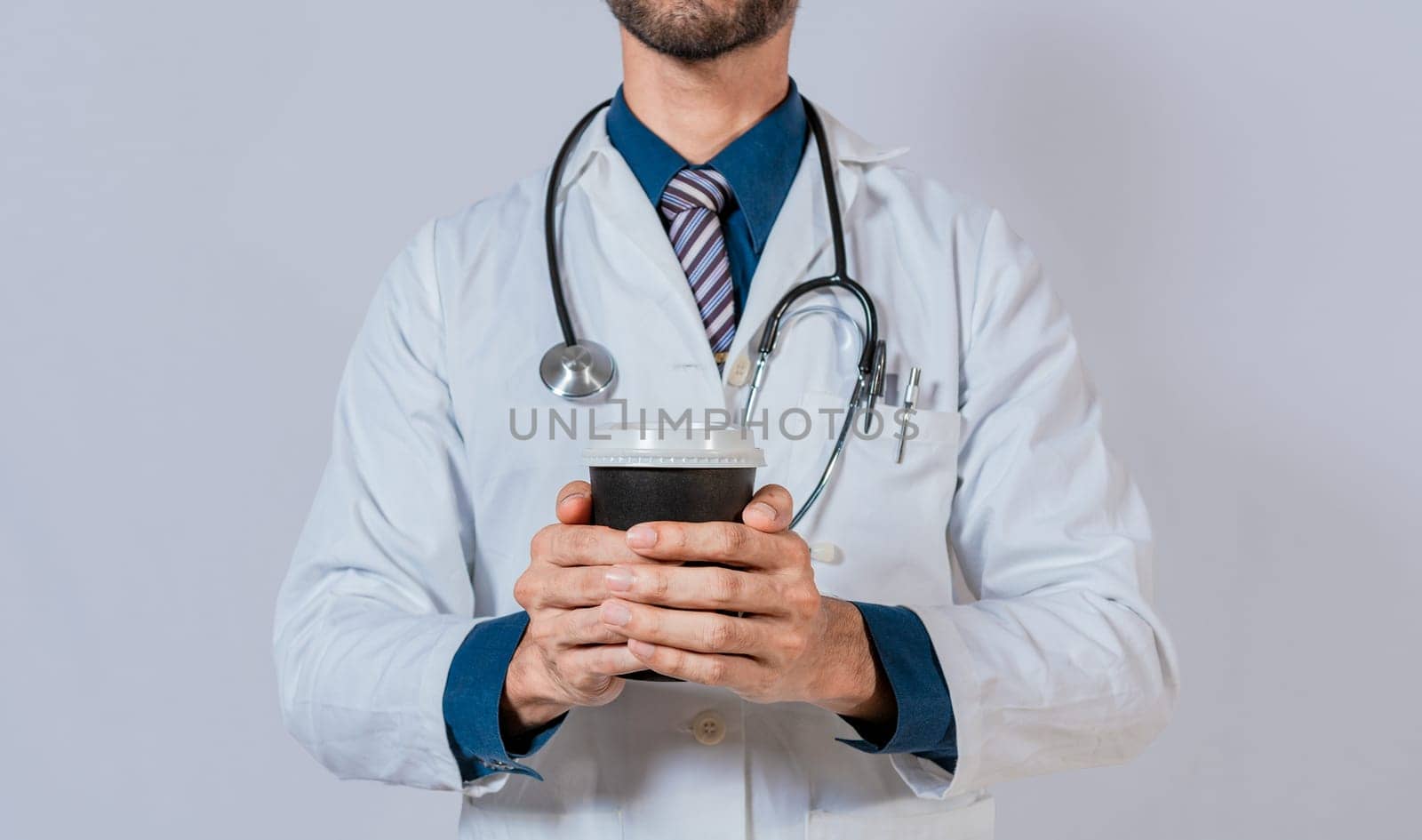 Young doctor holding a coffee to go isolated. Doctor hands holding paper coffee. Doctor holding takeaway coffee on isolated background by isaiphoto