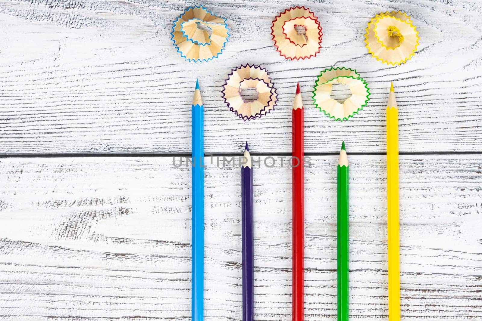 Five 5 colored, bright pencils for drawing drawings with wooden shavings are sharpened and lie on a wooden background, surface.