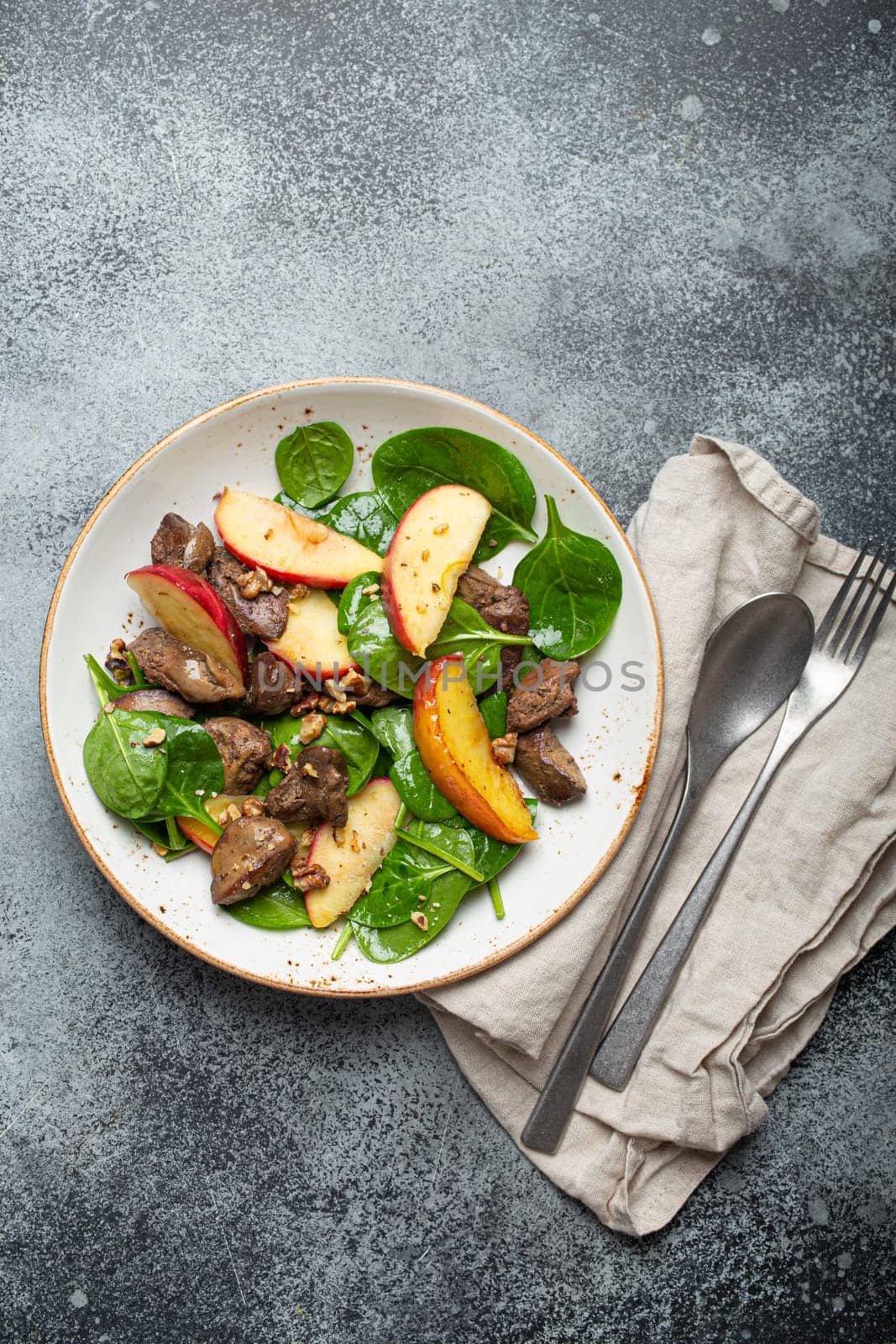 Healthy Salad with Iron Rich Ingredients Chicken Liver, Apples, Fresh Spinach and Walnuts on White Ceramic Plate, Grey Rustic Stone Background Top View.