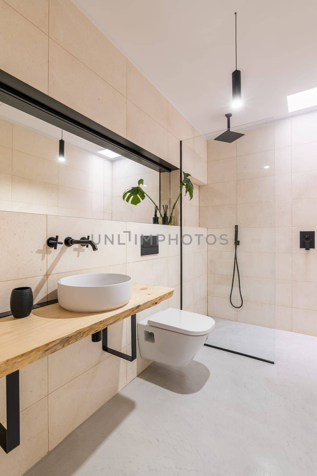 Loft style bathroom with toilet, big mirrors and sink and glass shower cabin with beige tile. The concept of renovation in a hotel or honeymoon room in a hostel. Copyspace.