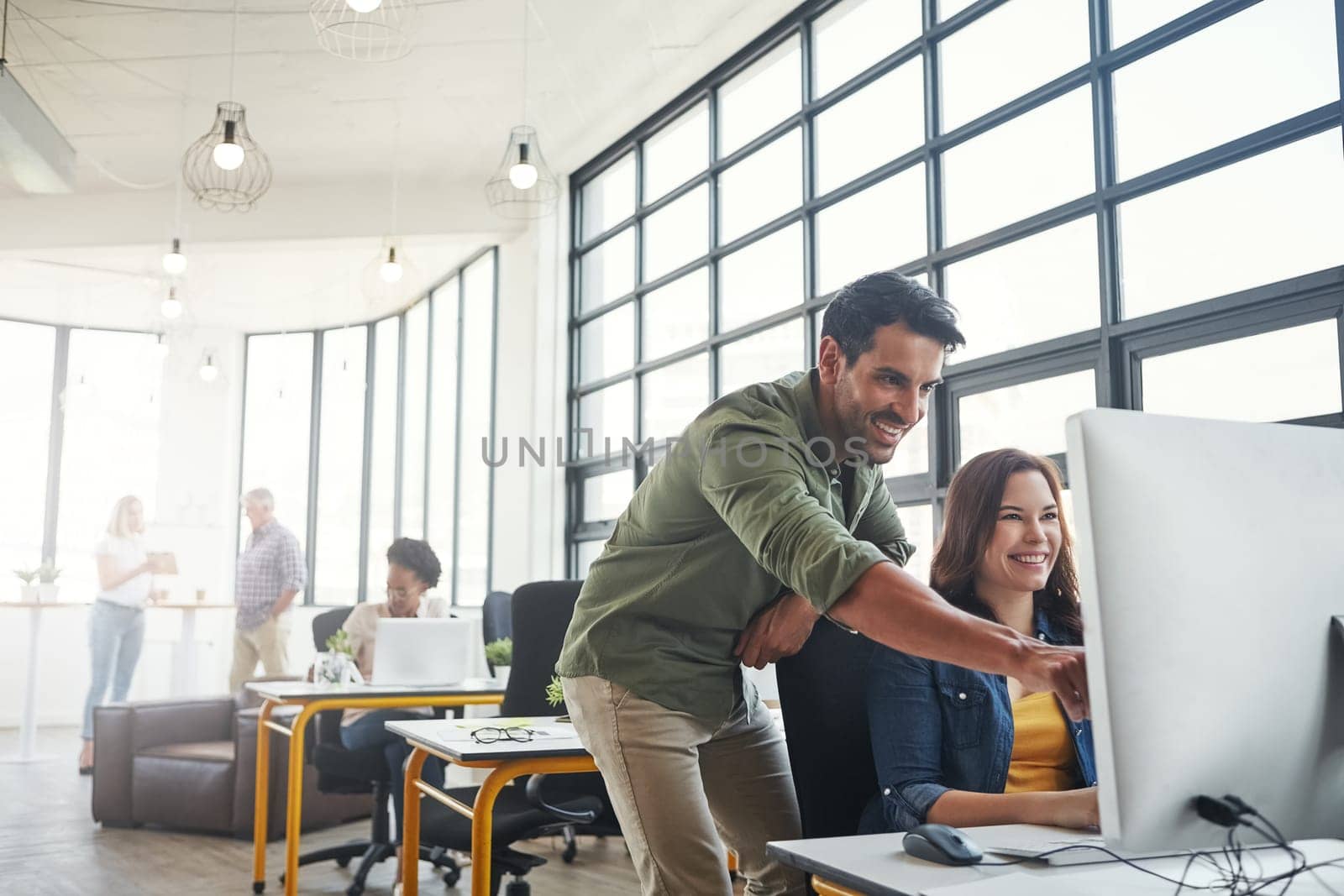 Designers must be technologically in tune with all changes. a male designer assisting his colleague at her desk. by YuriArcurs