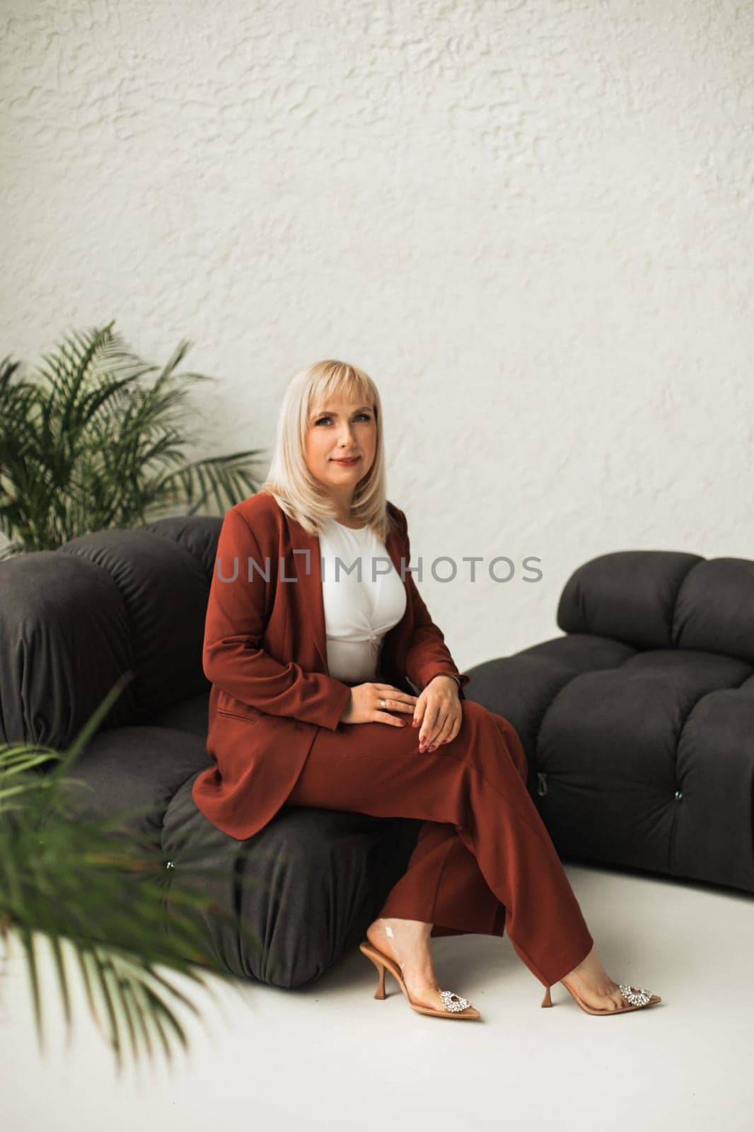 A fashionable woman with makeup in a teracote suit poses in the interior.