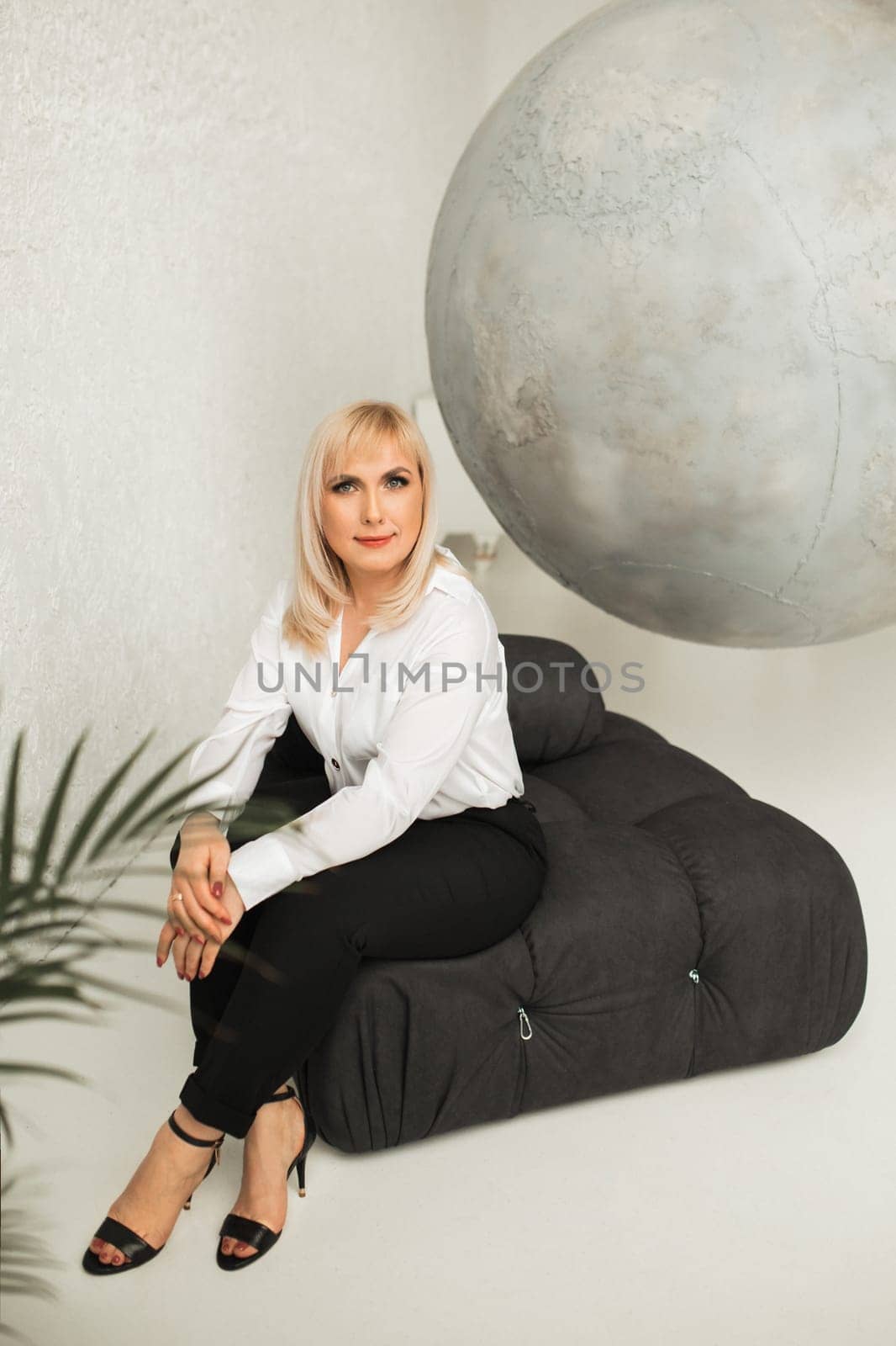 A fashionable woman In a white shirt and black pants poses in the interior.