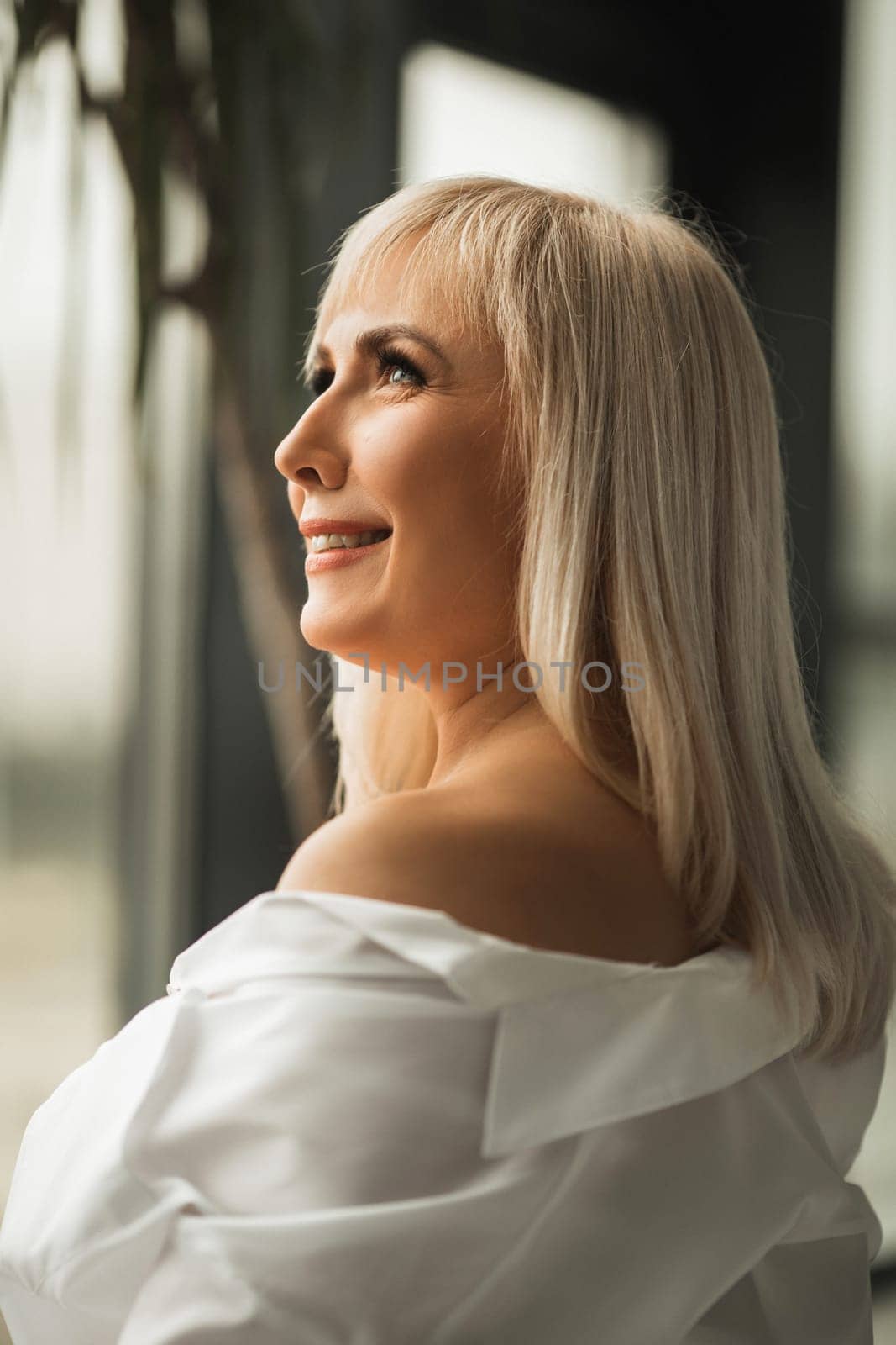 A fashionable woman in a white shirt poses in the interior.