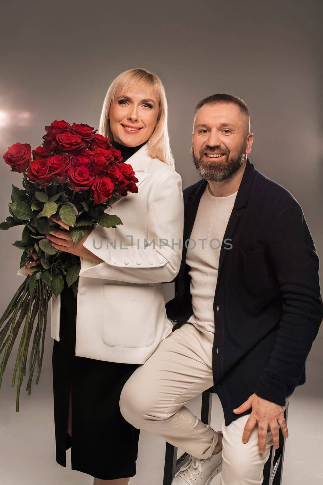 A man and a woman with flowers in their hands in strict clothes pose in the background in the studio.