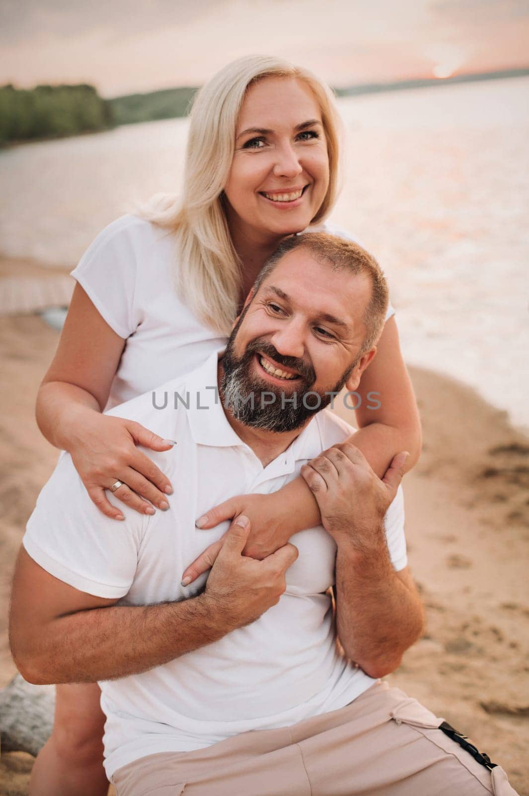 Happy married couple in shorts and T-shirts outside at sunset in summer by Lobachad