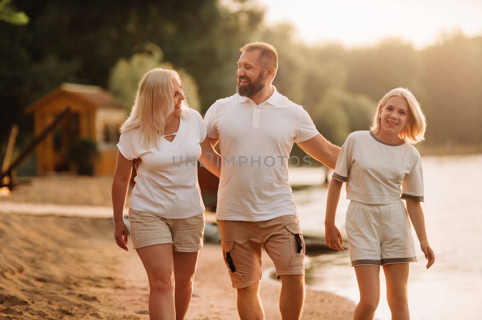 Happy family - father, mother and daughter in light clothes having fun together on the beach in summer.
