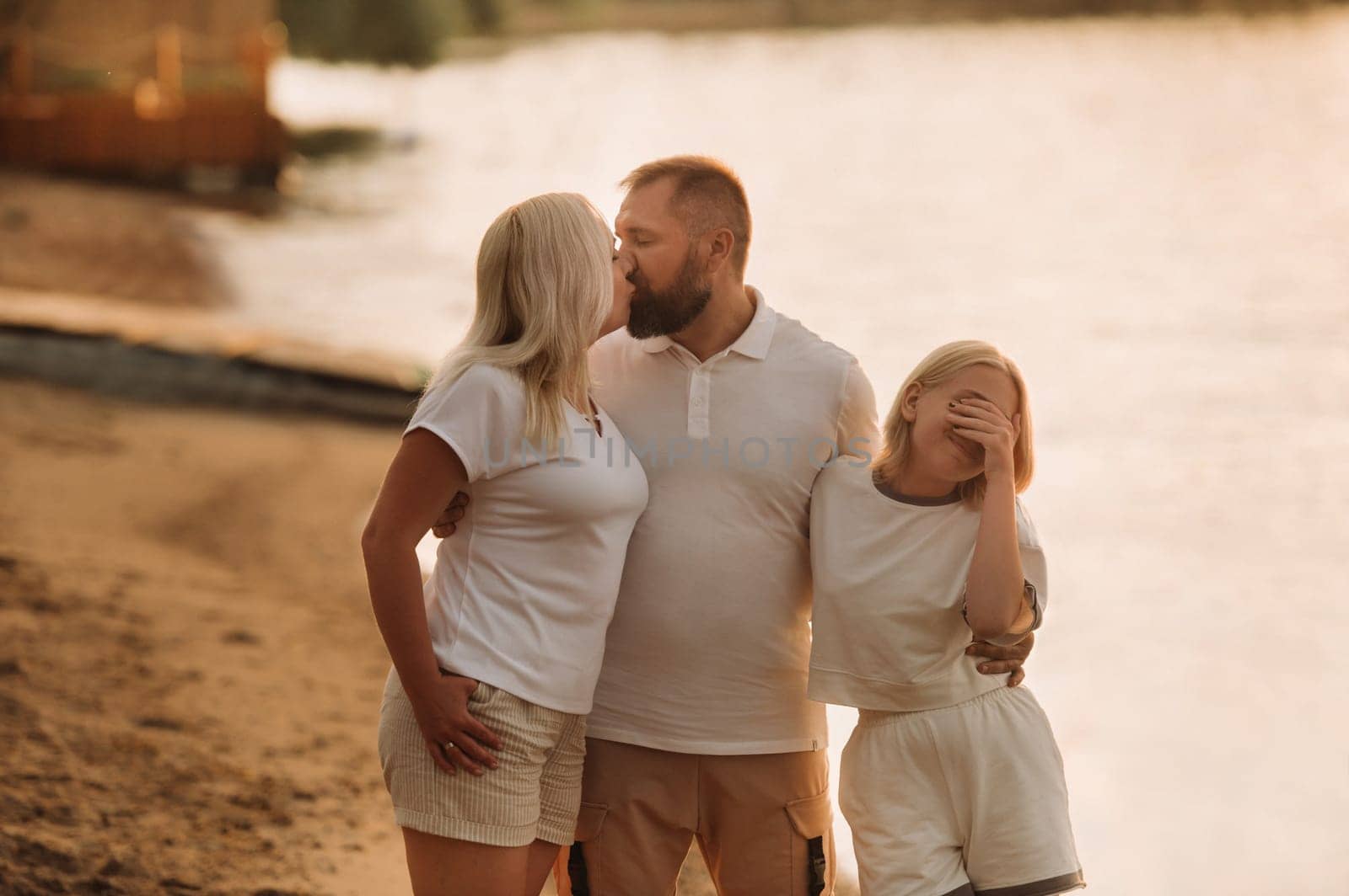 Happy family - father, mother and daughter in light clothes having fun together on the beach in summer by Lobachad