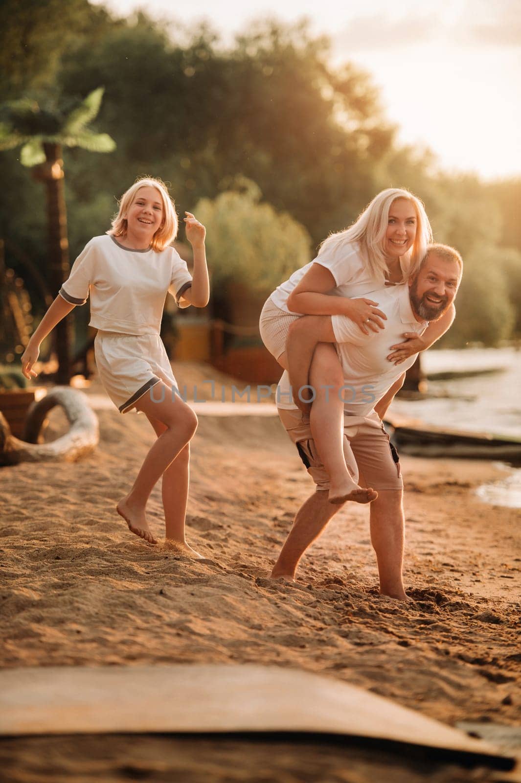 Happy family - father, mother and daughter in light clothes having fun together on the beach in summer.