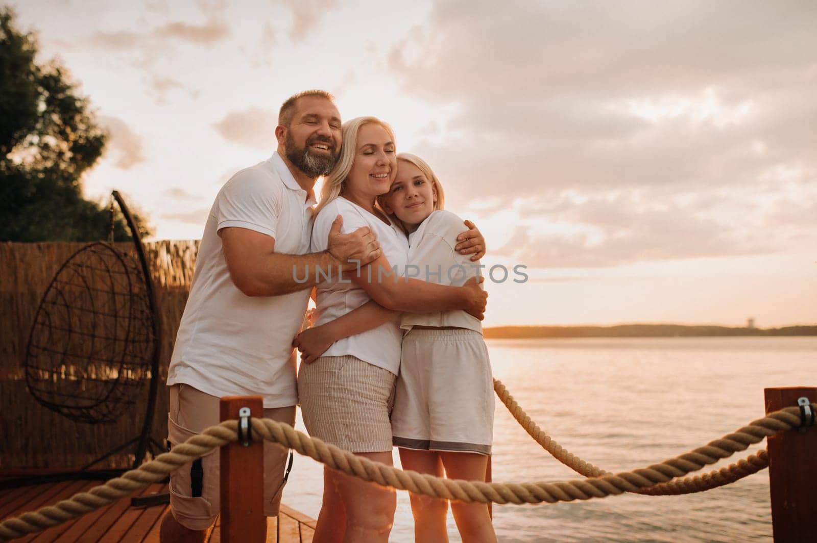 Happy family - father, mother and daughter in light clothes hugging together on the beach in summer by Lobachad