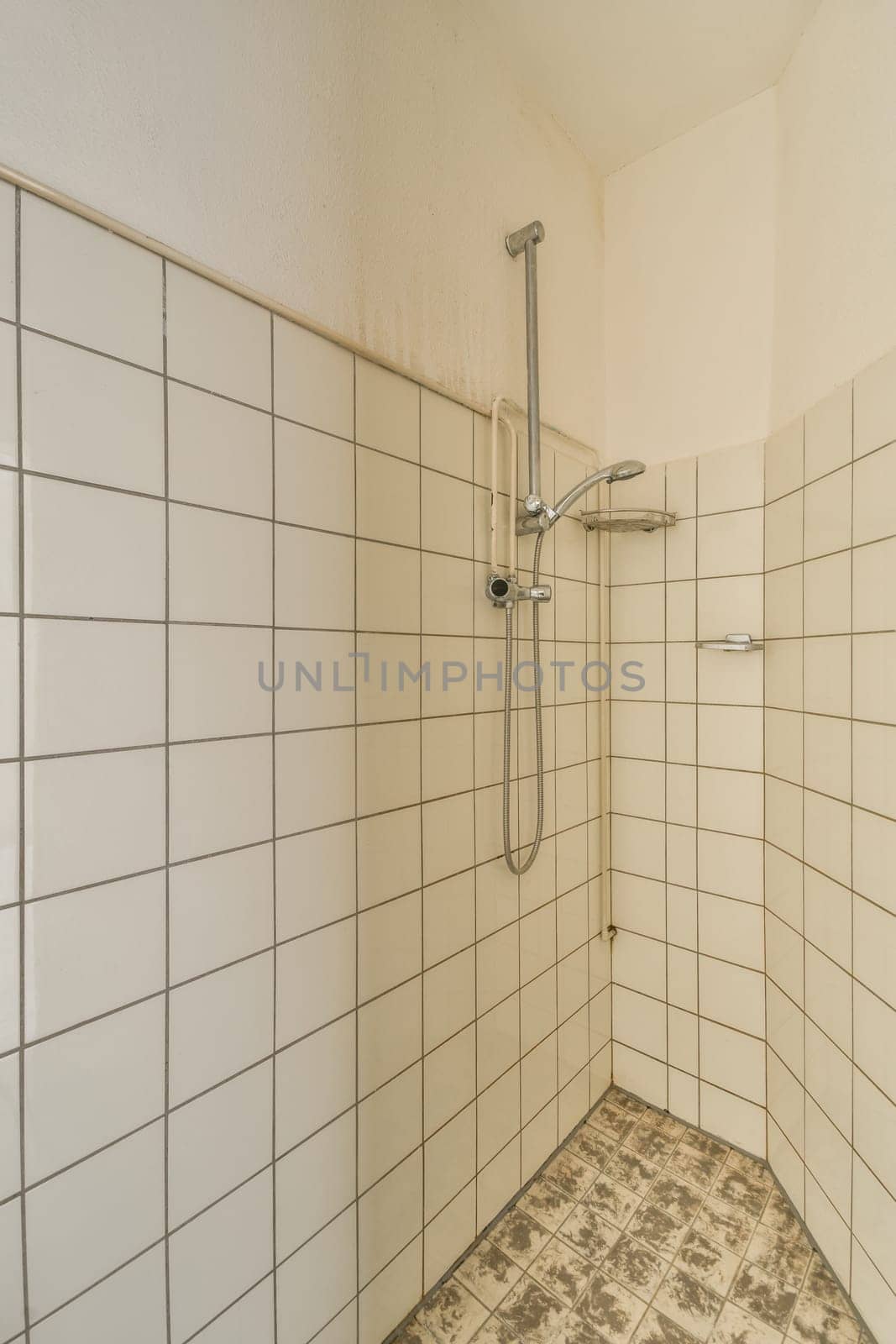 a bathroom with tile on the floor and shower head mounted to the wall, in front of white tiled walls