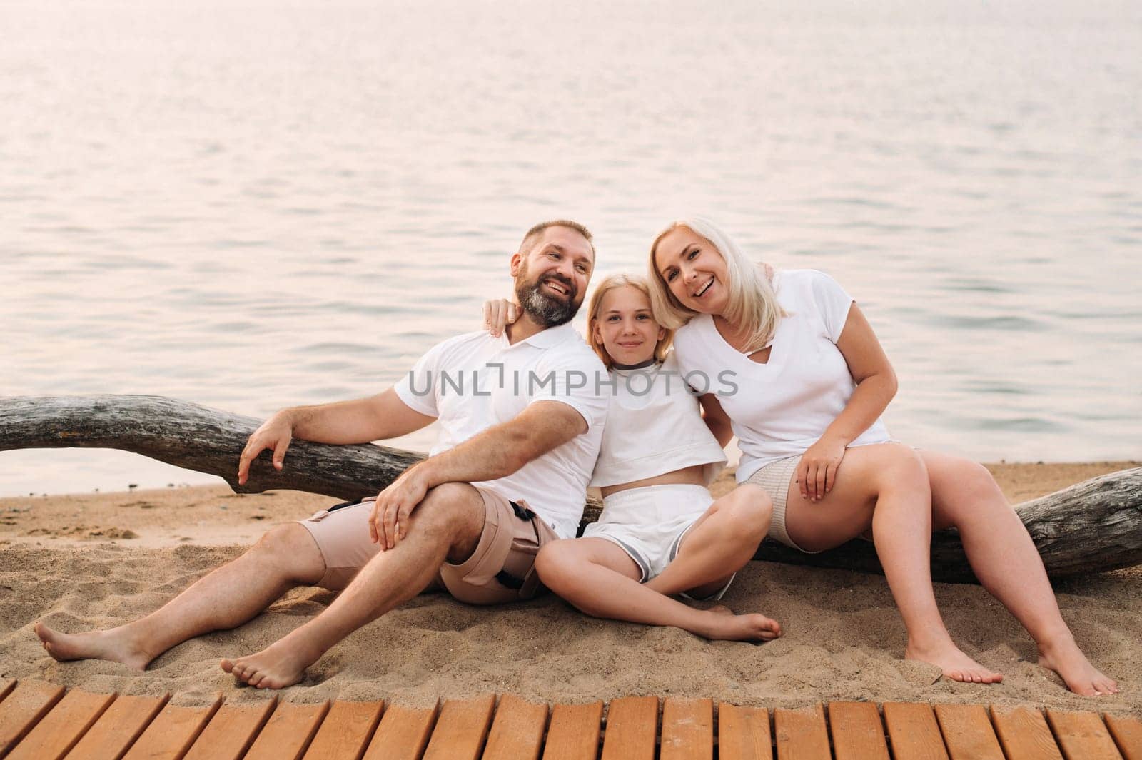 Happy family of three relaxing sitting on the beach after sunset by Lobachad