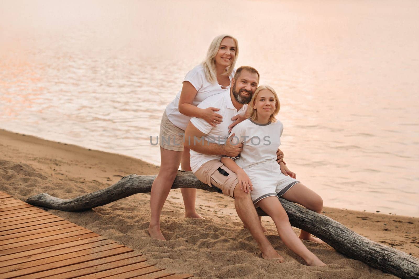 Happy family of three relaxing sitting on the beach after sunset.