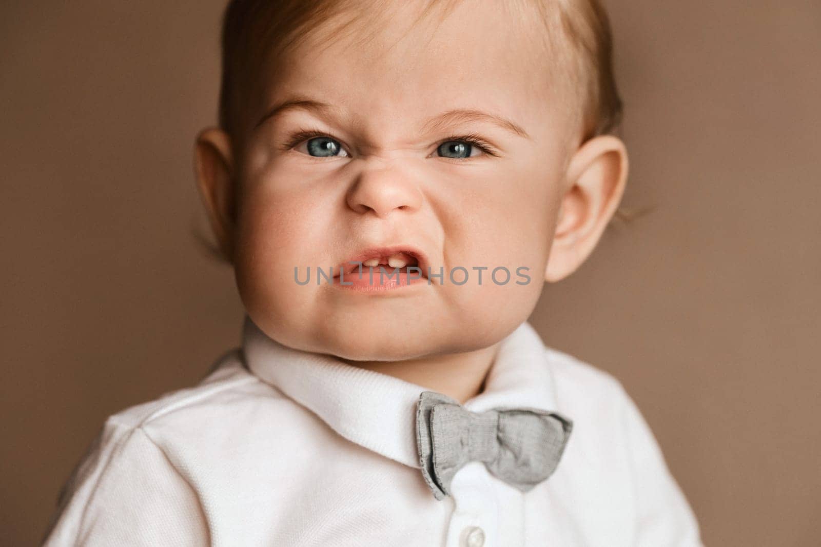 Portrait of a little boy in a white shirt with a bow tie grimacing on camera by Lobachad