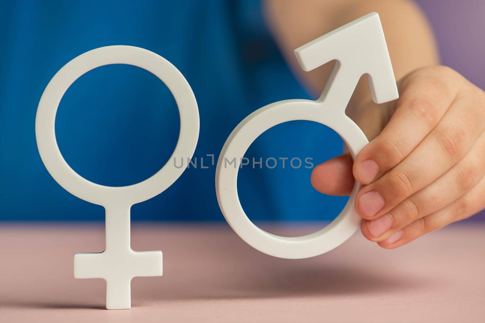 The concept of gender equality. Symbol of female and male gender in hand as a symbol of equality of rights. On a purple background in a blue t-shirt with copy space by SERSOL