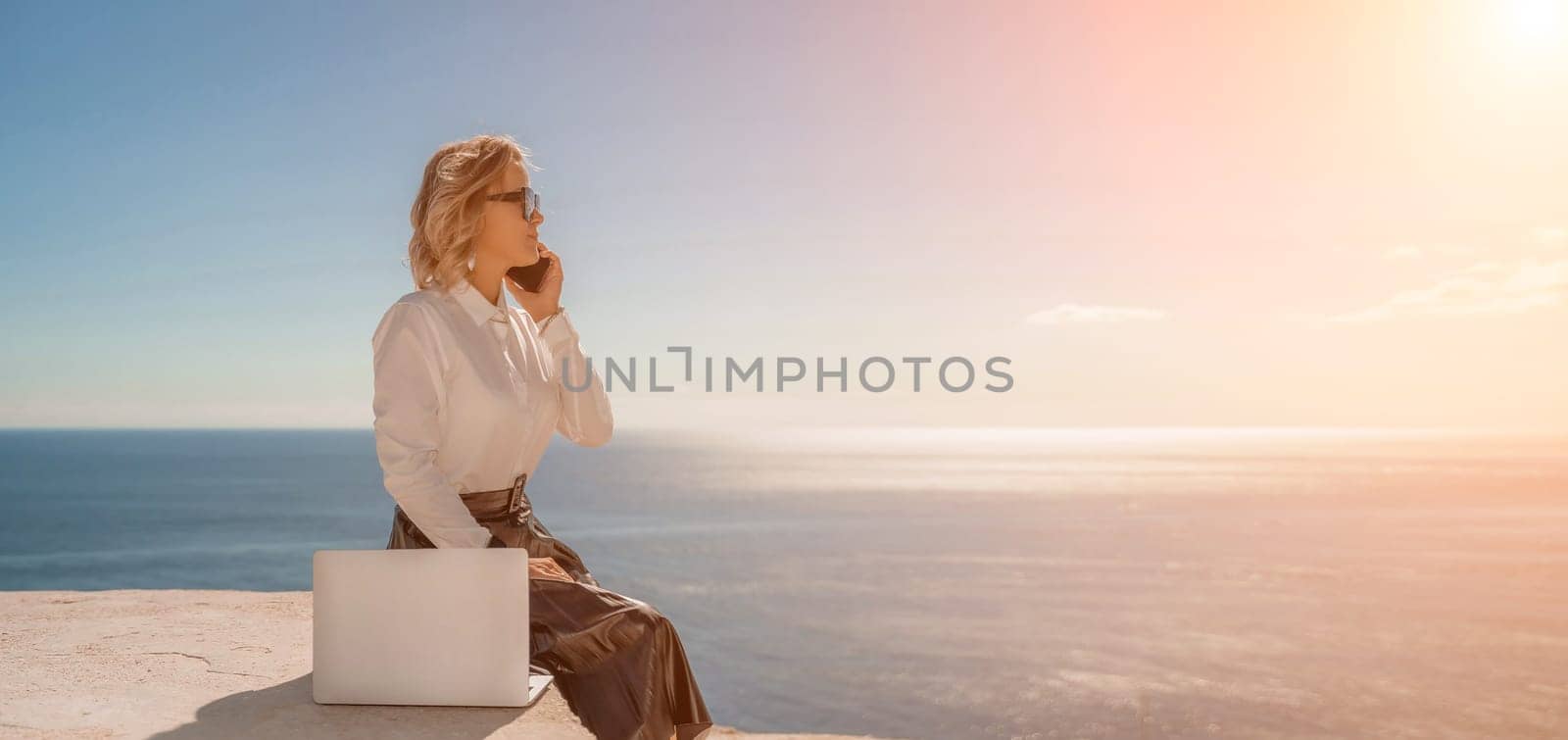 Business woman on nature in white shirt and black skirt. She works with an iPad in the open air with a beautiful view of the sea. The concept of remote work