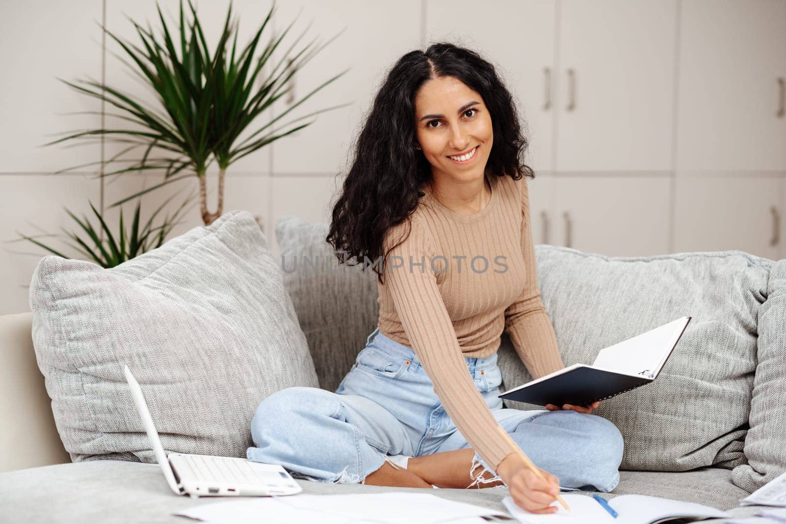 Happy Brunette Business Lady Using Laptop Smiling To Camera Posing Wearing Working Sitting At Workplace In Home Office. Successful Entrepreneurship And Career Concept. Smiling arab woman taking notes