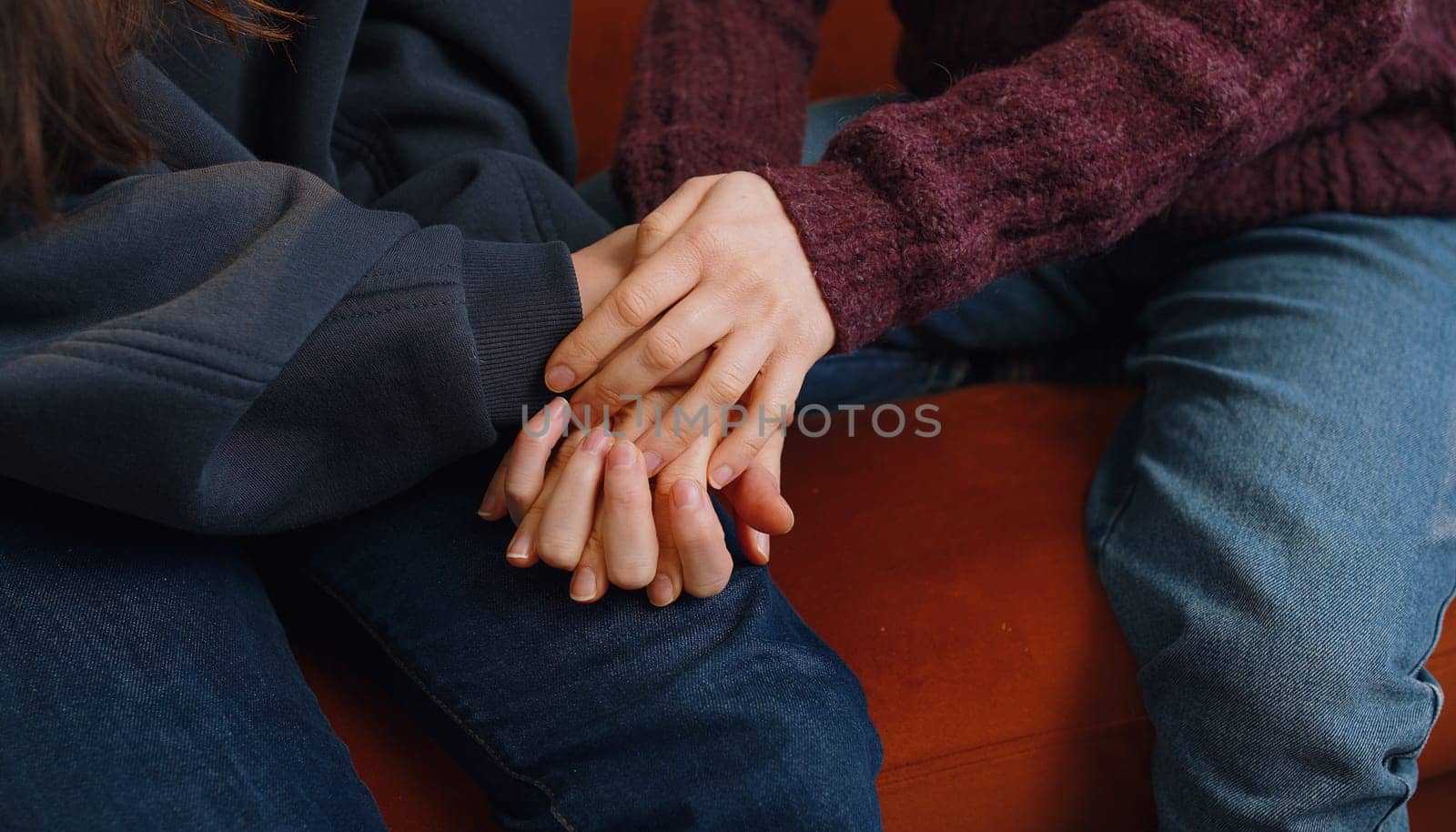 Close-up of two lesbian women family couple, girls friends holding caressing hands together, showing love to each other at home room sitting on couch. Woman relationship, LGBT same-sex people concept