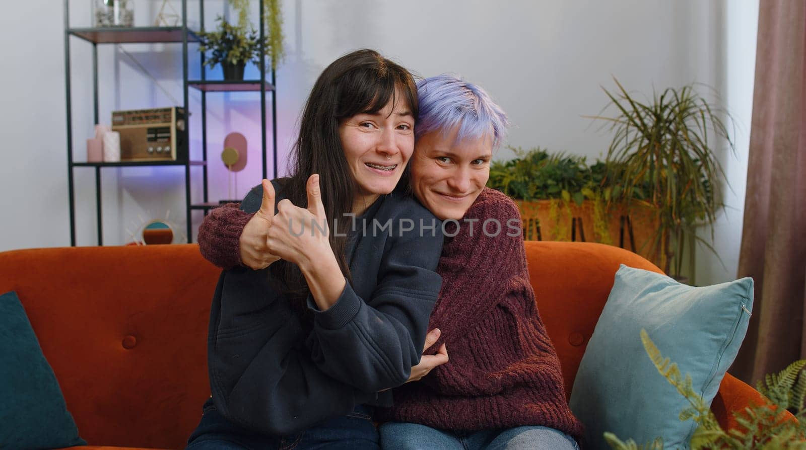 Like. Happy two young lesbian women family couple or girls friends looking approvingly at camera showing thumbs up, like sign something good positive feedback at home living room. LGBT people concept