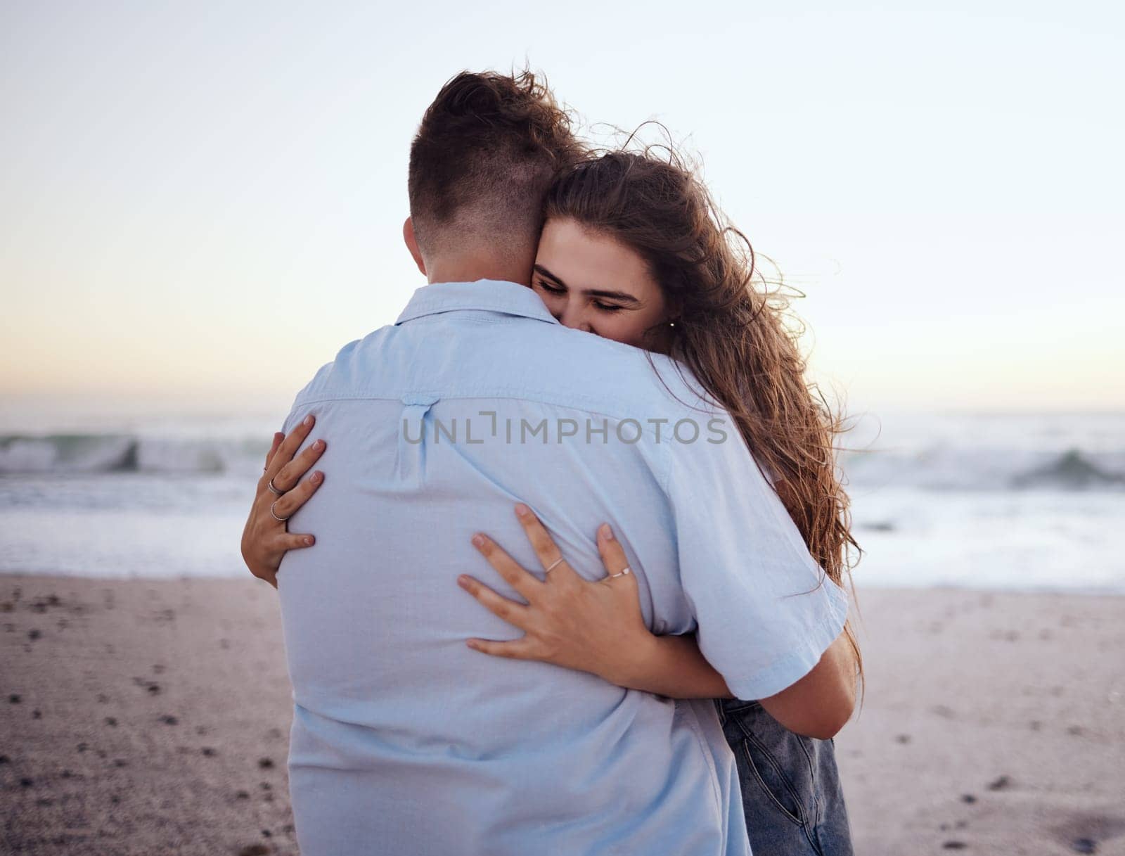 Love, hug and romance with a couple on the beach during a date on the sand by the sea or ocean at sunset. Summer, nature and travel with a young man and woman hugging on the coast while dating.
