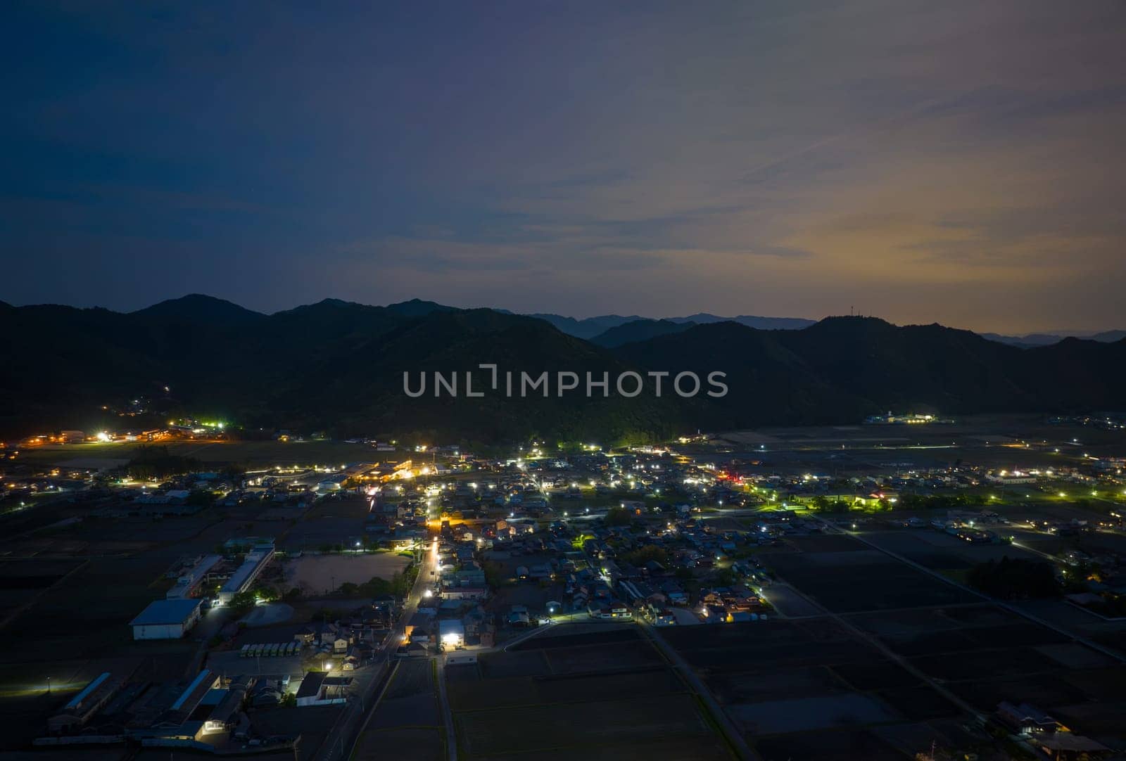 Lights from houses and streets in small town at foot of mountain range at twilight. High quality photo