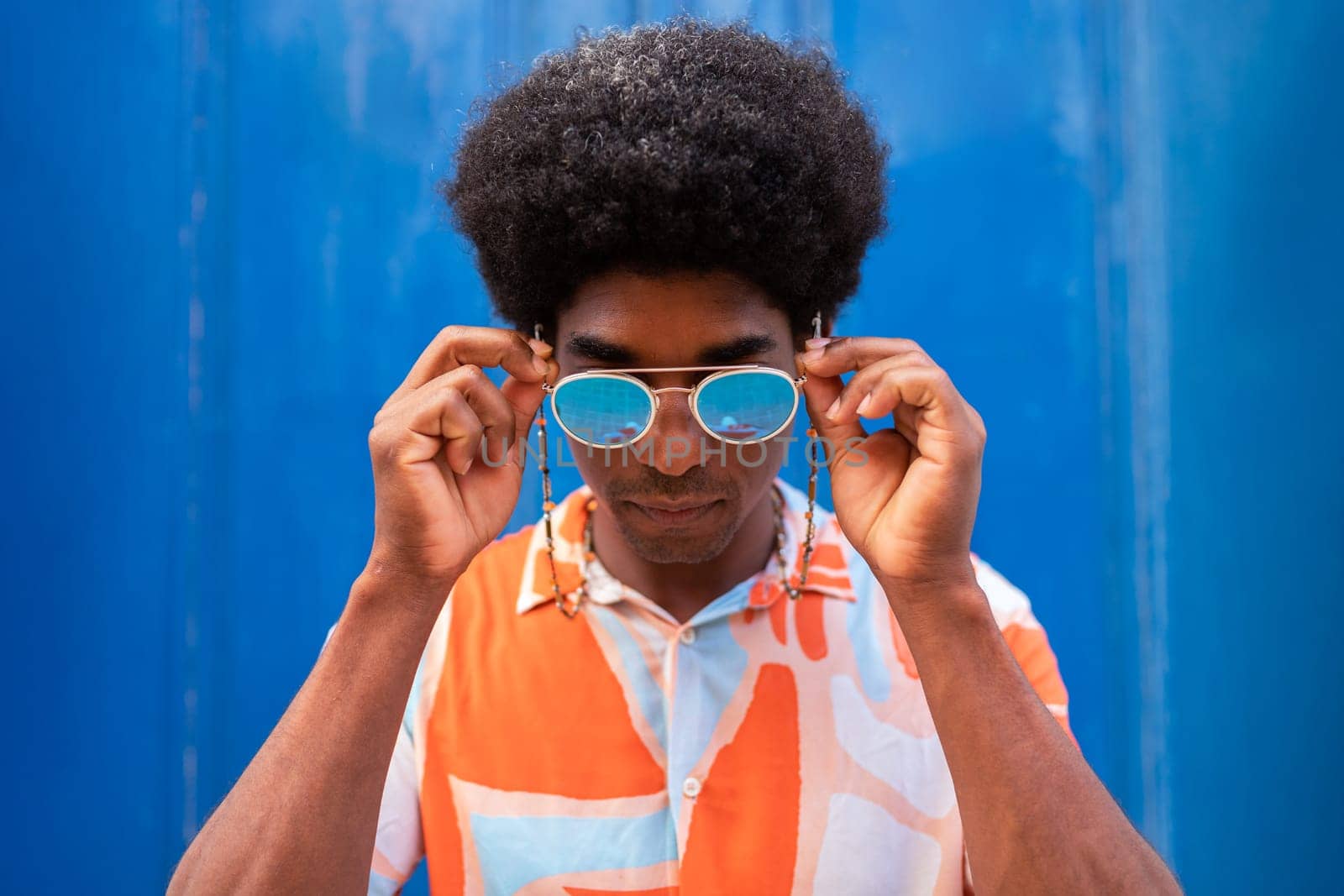 Cool and confident young African American man putting on sunglasses outdoors. by Hoverstock