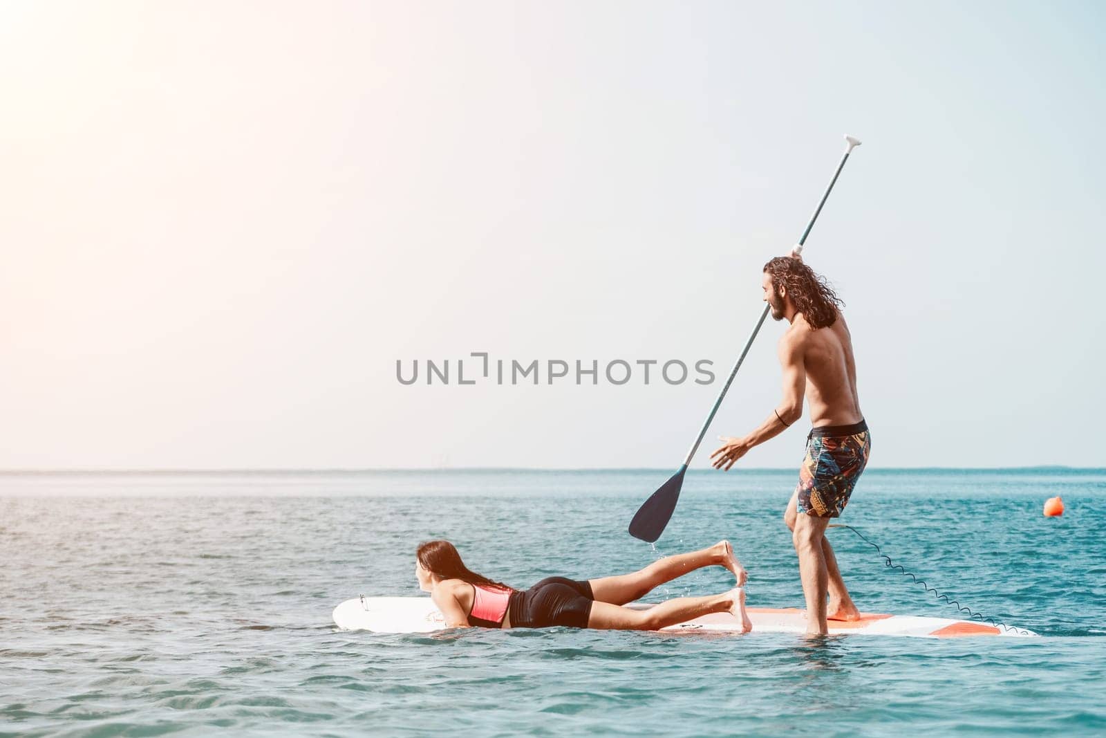 Sea woman and man on sup. Silhouette of happy young woman and man, surfing on SUP board, confident paddling through water surface. Idyllic sunset. Active lifestyle at sea or river