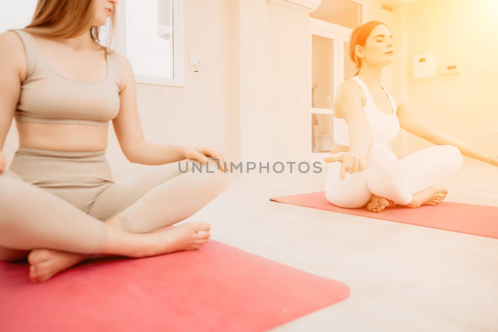 Group of young womans fitness instructor in Sportswear Leggings and Tops, stretching in the gym before pilates, on a yoga mat near the large window on a sunny day, female fitness yoga routine concept.