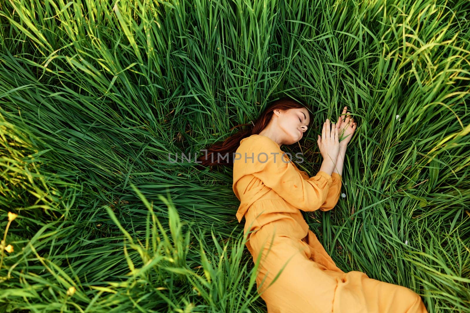 a relaxed woman enjoys summer lying in the tall green grass with her eyes closed. Photo taken from above by Vichizh