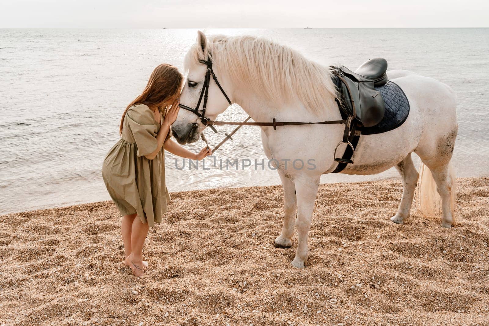 A white horse and a woman in a dress stand on a beach, with the sky and sea creating a picturesque backdrop for the scene